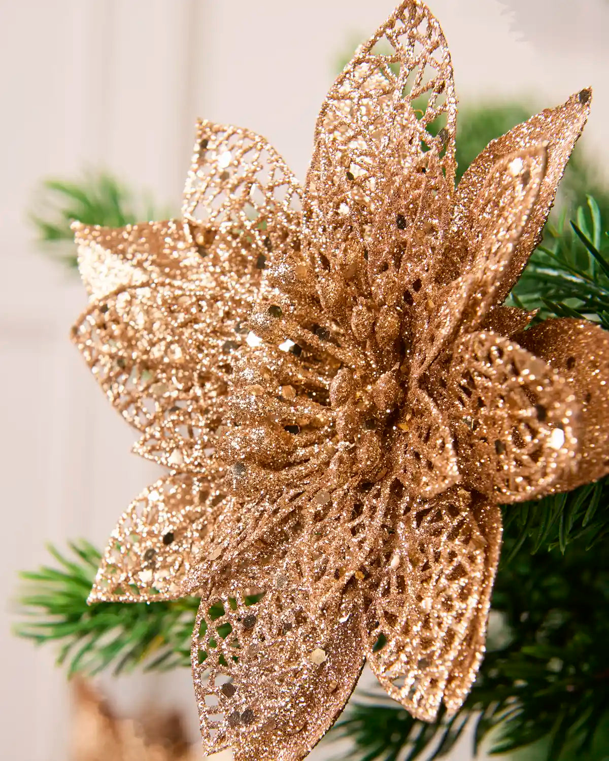 Close-up of a Rose Gold glitter artificial poinsettia flower showing its densely textured, sparkling petals.
