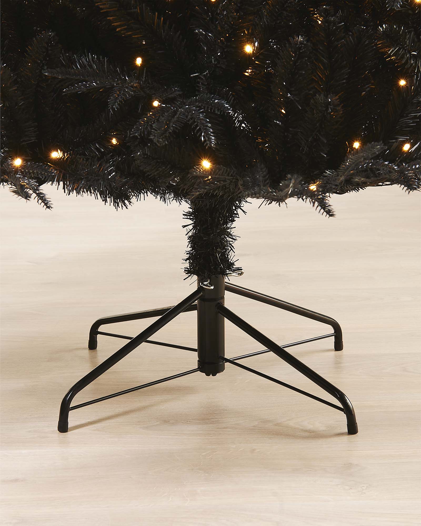 Close-up of a black Christmas tree with silver stars on a neutral background.