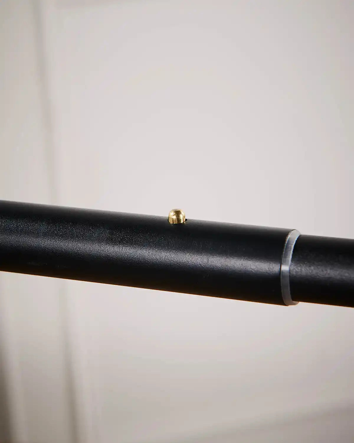 Close-up of a black rod with a small gold clip on a light grey background