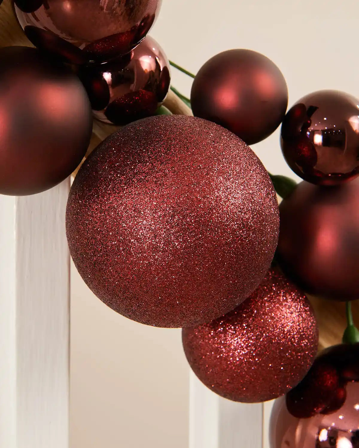 Close-up of a burgundy bauble garland on a staircase banister against a cream wall
