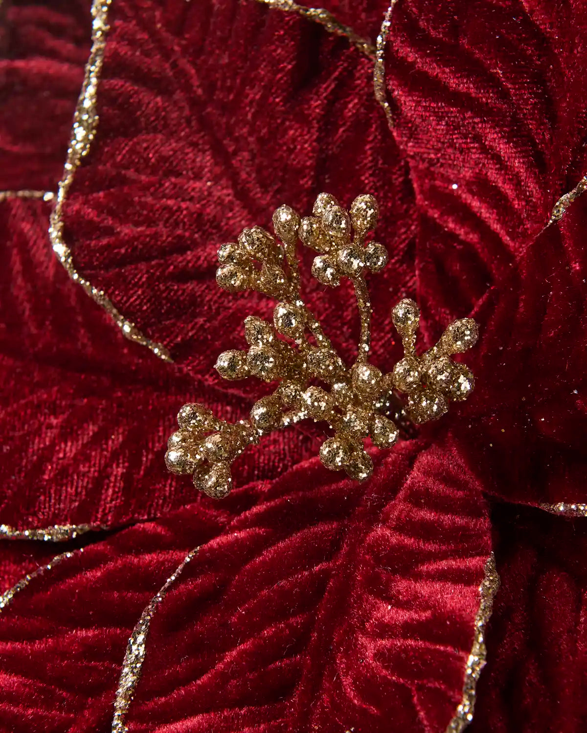 Close-up of a burgundy velvet-look artificial poinsettia featuring glittered gold edging and a cluster of gold glitter berries at the center.
