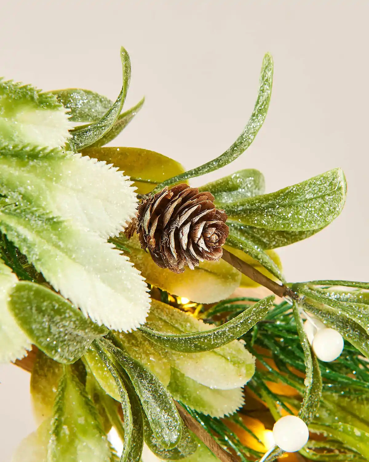 Close-up of a decorative arrangement with green leaves and a pine cone on a light background