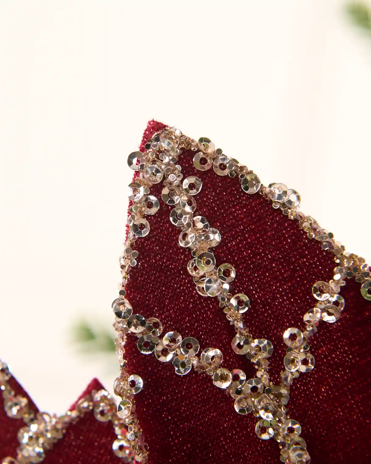 Close-up of a deep burgundy velvet fabric with intricate gold beading and clear rhinestone embellishments.