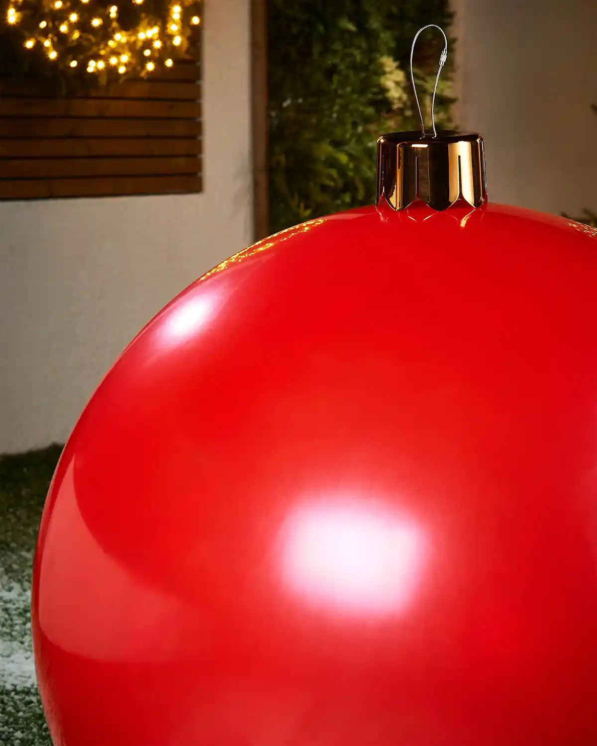 Close-up of a extra large red Christmas inflatable bauble with gold cap against a blurred indoor background
