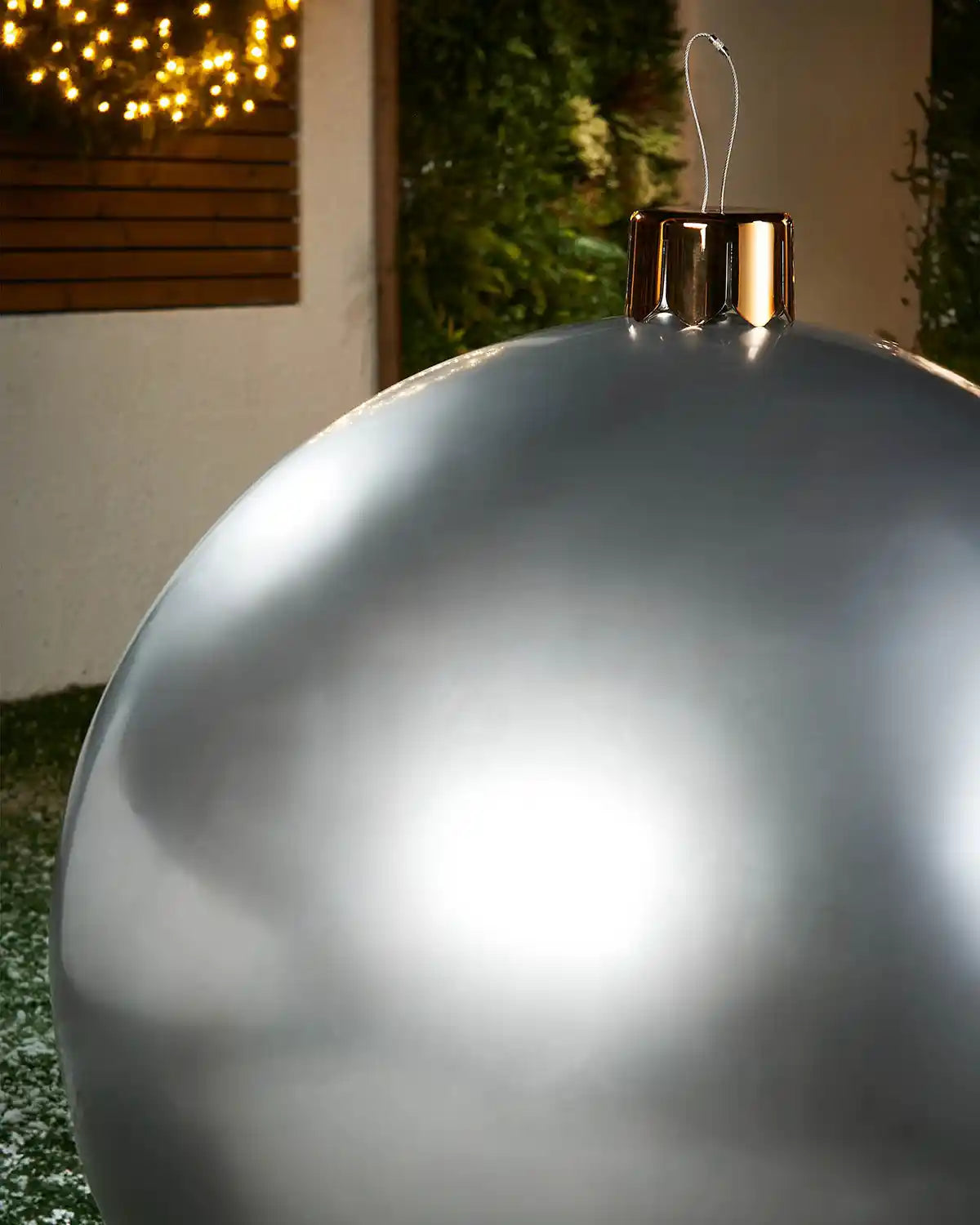 Close-up of a extra large silver Christmas inflatable bauble with gold cap against a blurred indoor background
