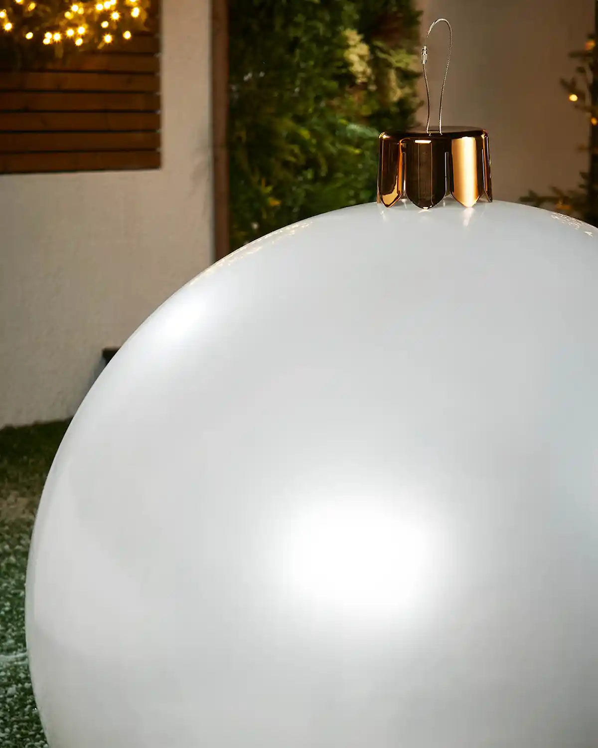 Close-up of a extra large white Christmas inflatable bauble with gold cap against a blurred indoor background
