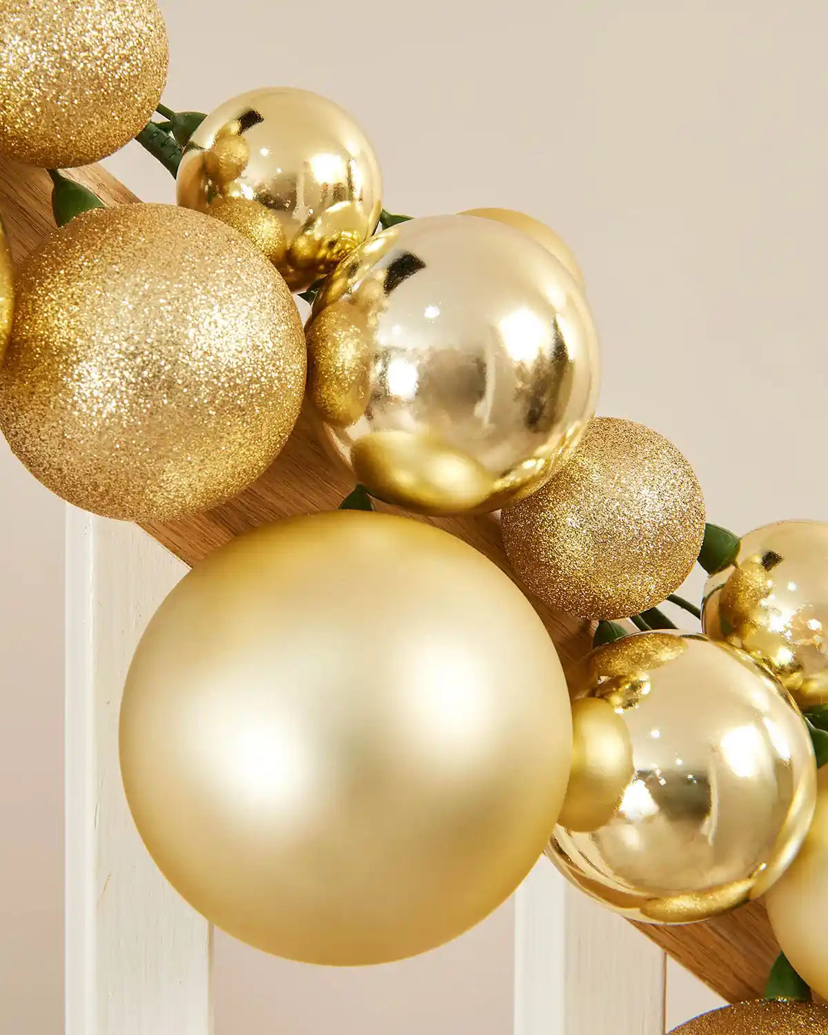 Close-up of a gold bauble garland on a staircase banister against a cream wall