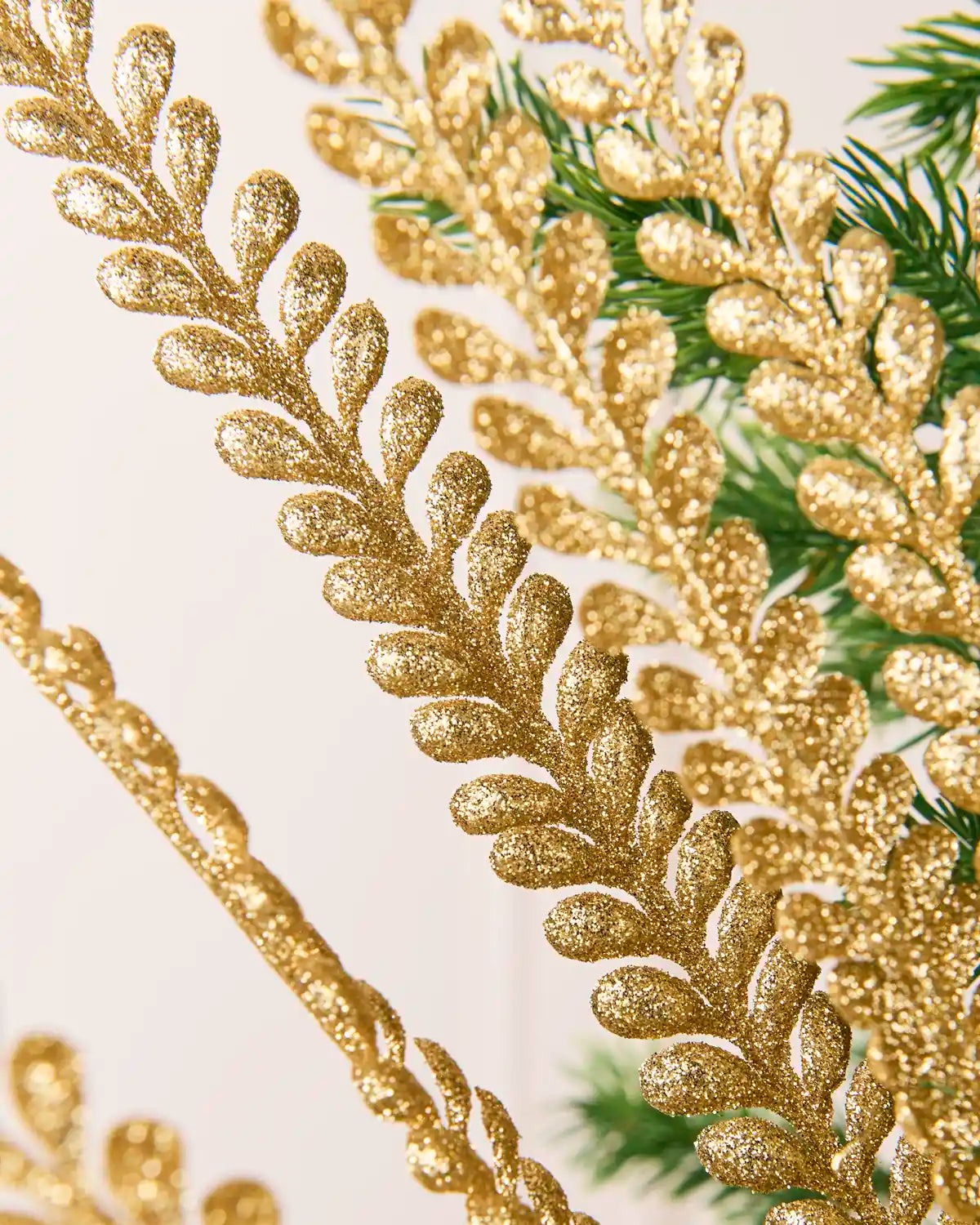 Close-up of a gold glitter leaf spray detailing glitter-covered leaves and Christmas tree branches  in the background