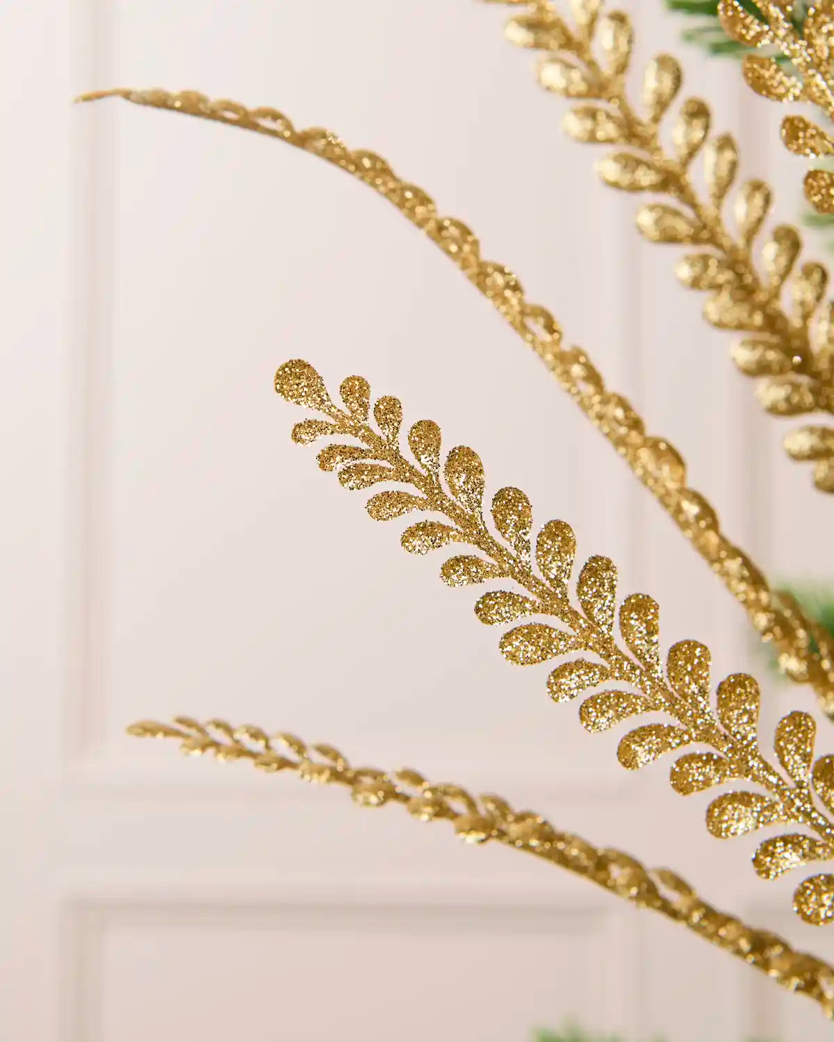 Close-up of a gold glitter leaf spray showing a curved branch covered in sparkling gold glitter leaves against a cream background