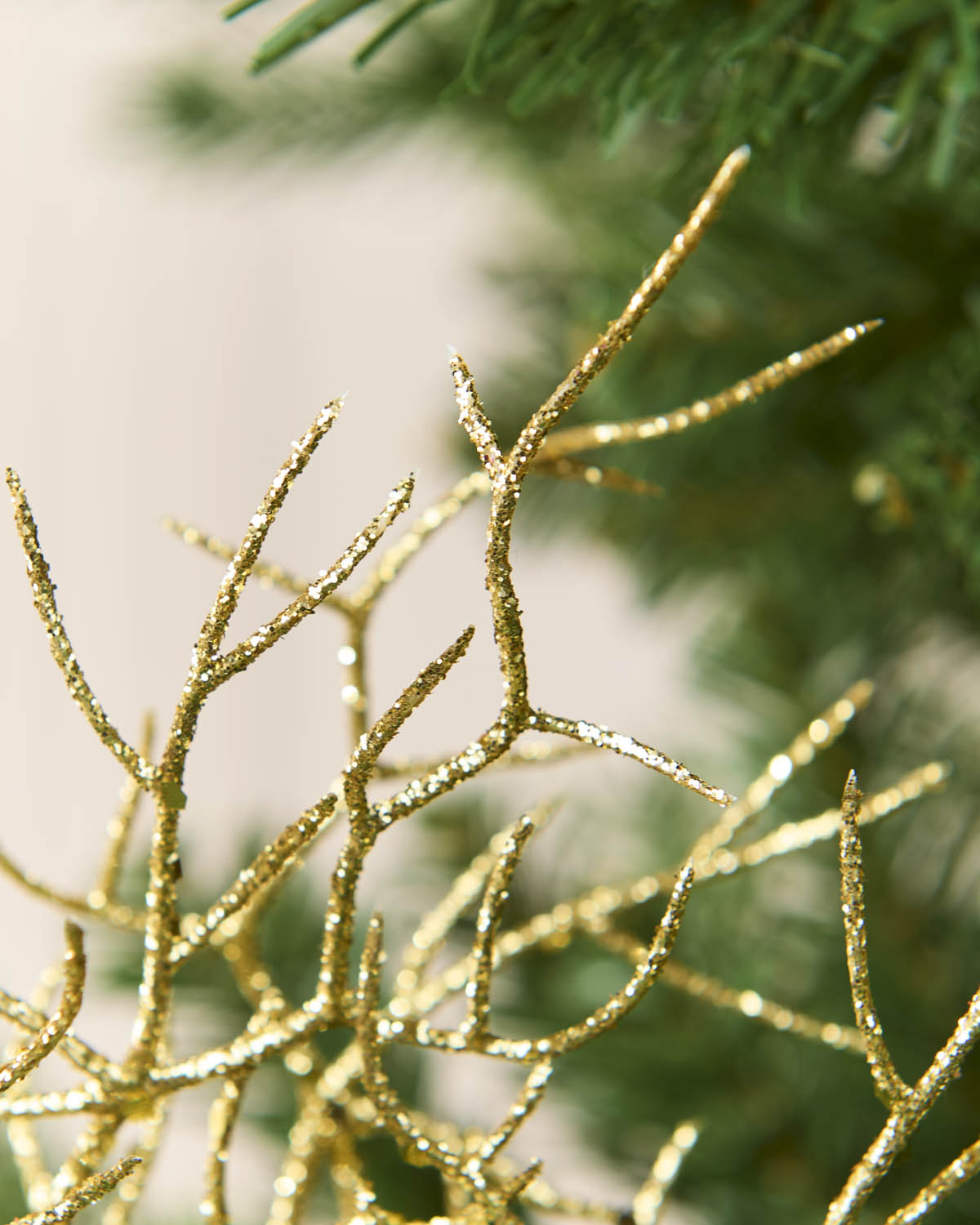 Close-up of a gold glittery branch or decorative twig ornament against a soft-focus background with green pine needles.