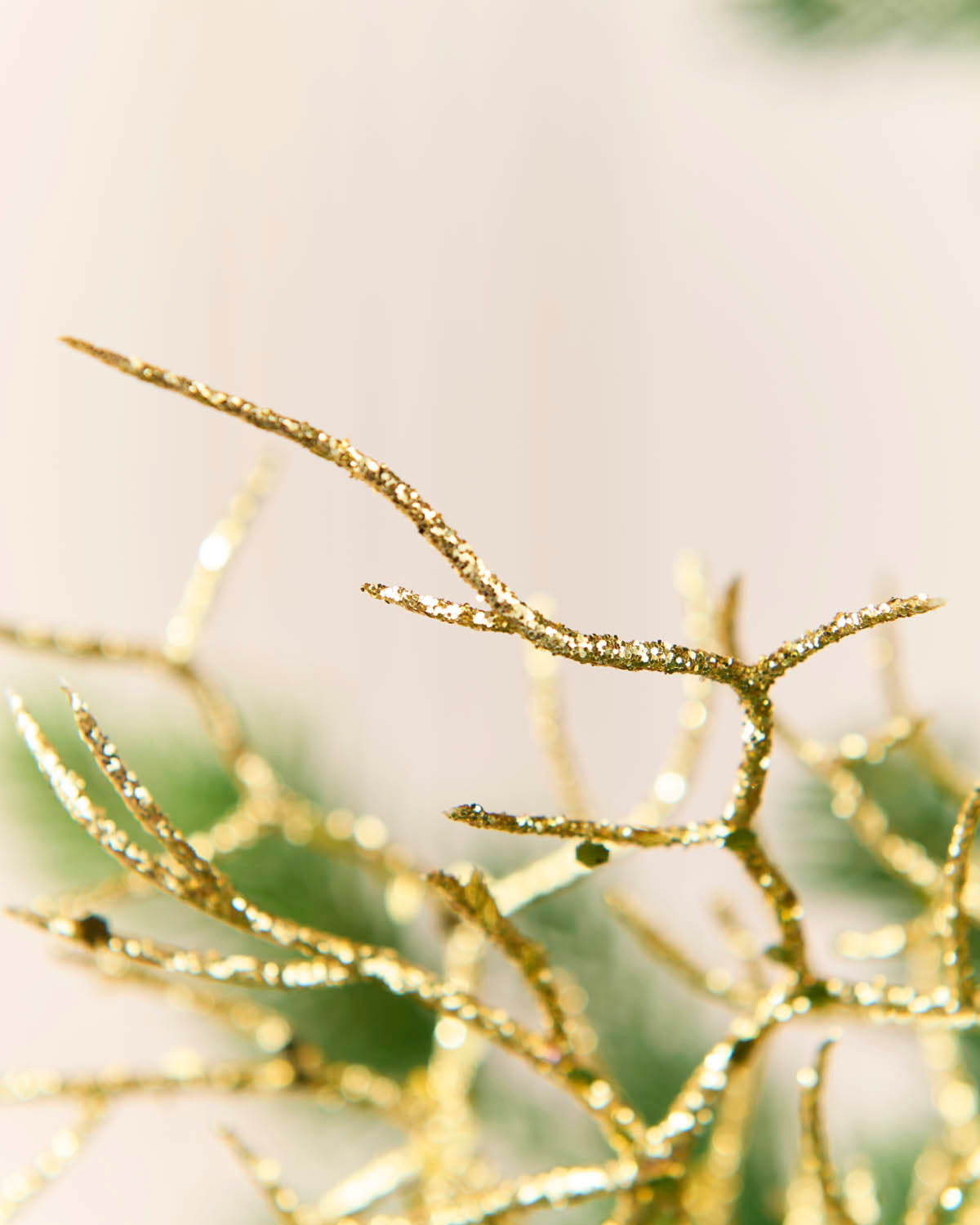 Close-up of a gold glittery decorative branch or coral-like ornament against a soft warm beige background with blurred green bokeh.