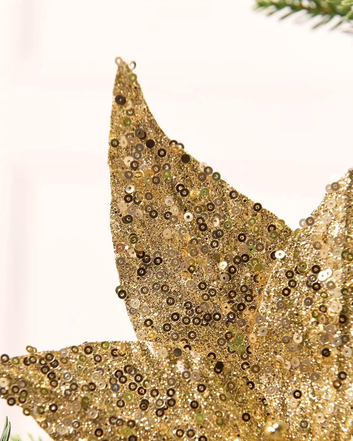 Close-up of a gold sequined decorative poinsettia ornament with shimmering metallic details against a soft light background.