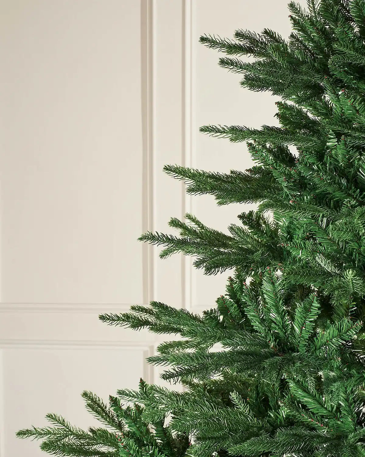 Close-up of a green artificial Christmas PVC and PE tips tree against a cream wall.