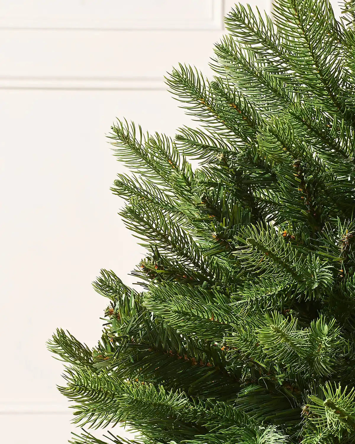 Close-up of a green artificial Christmas tree branch on a cream background