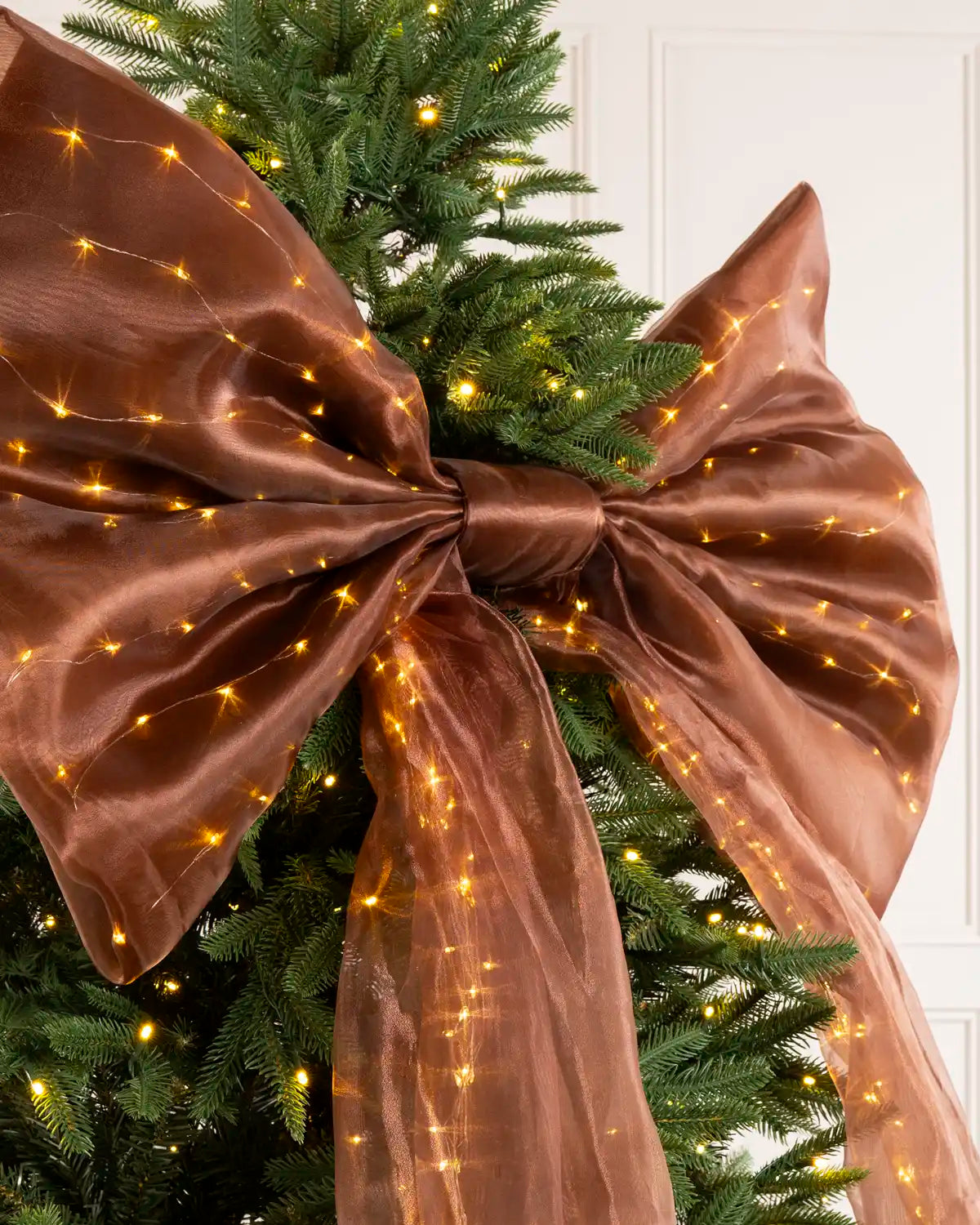 Close-up of a large espresso brown Christmas bow with warm white lights woven through the fabric.