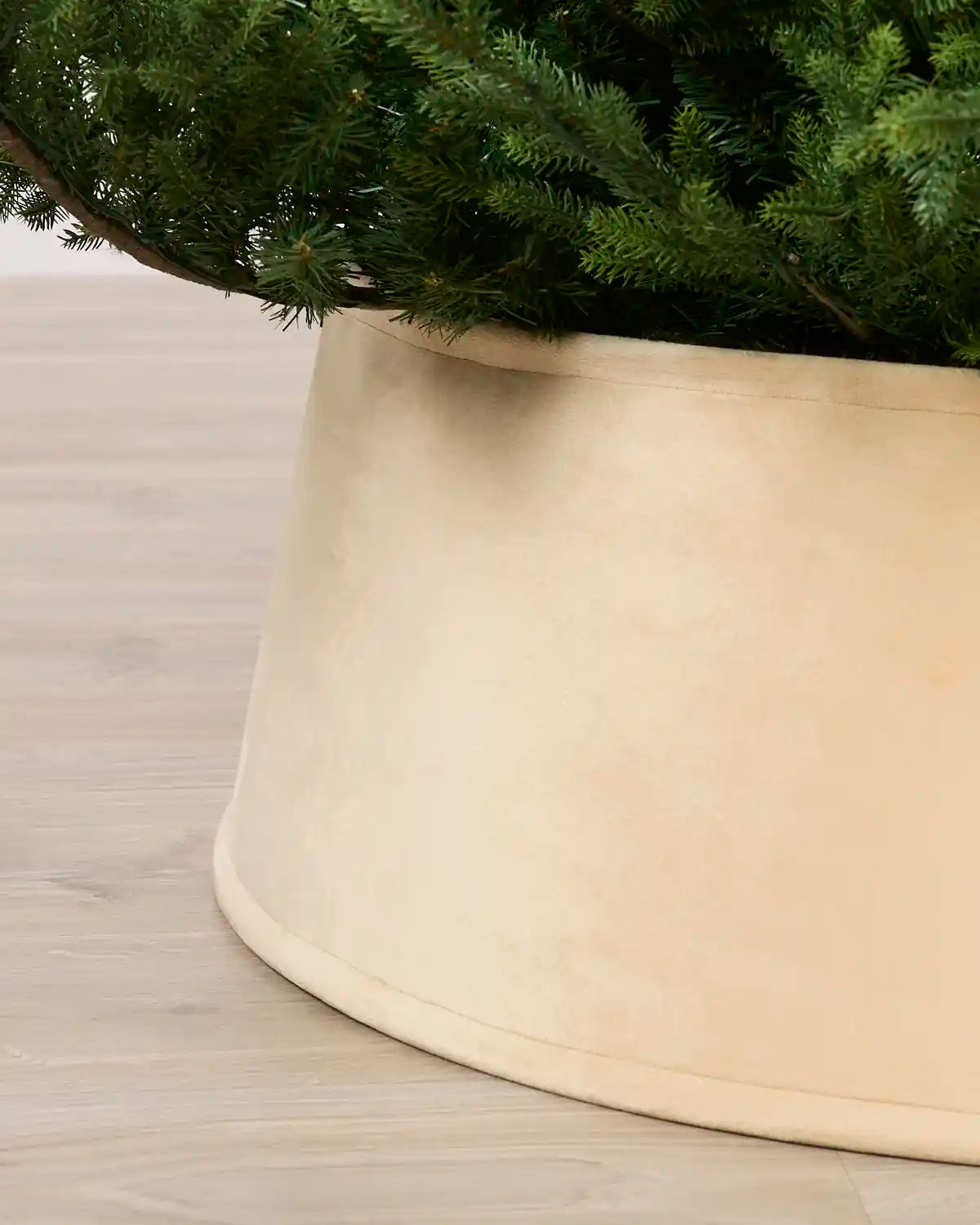 Close-up of a large latte coloured fabric tree skirt holding a green Christmas tree on a light wood floor.