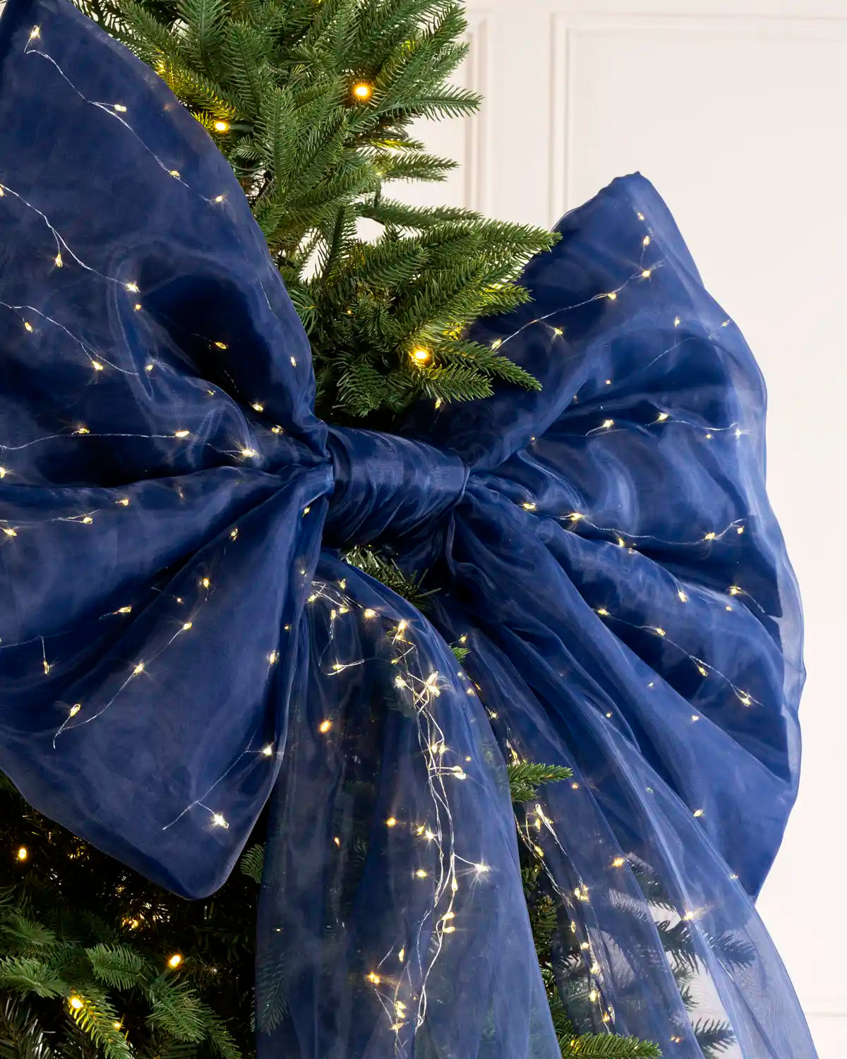 Close-up of a large navy blue Christmas bow with warm white lights woven through the fabric.