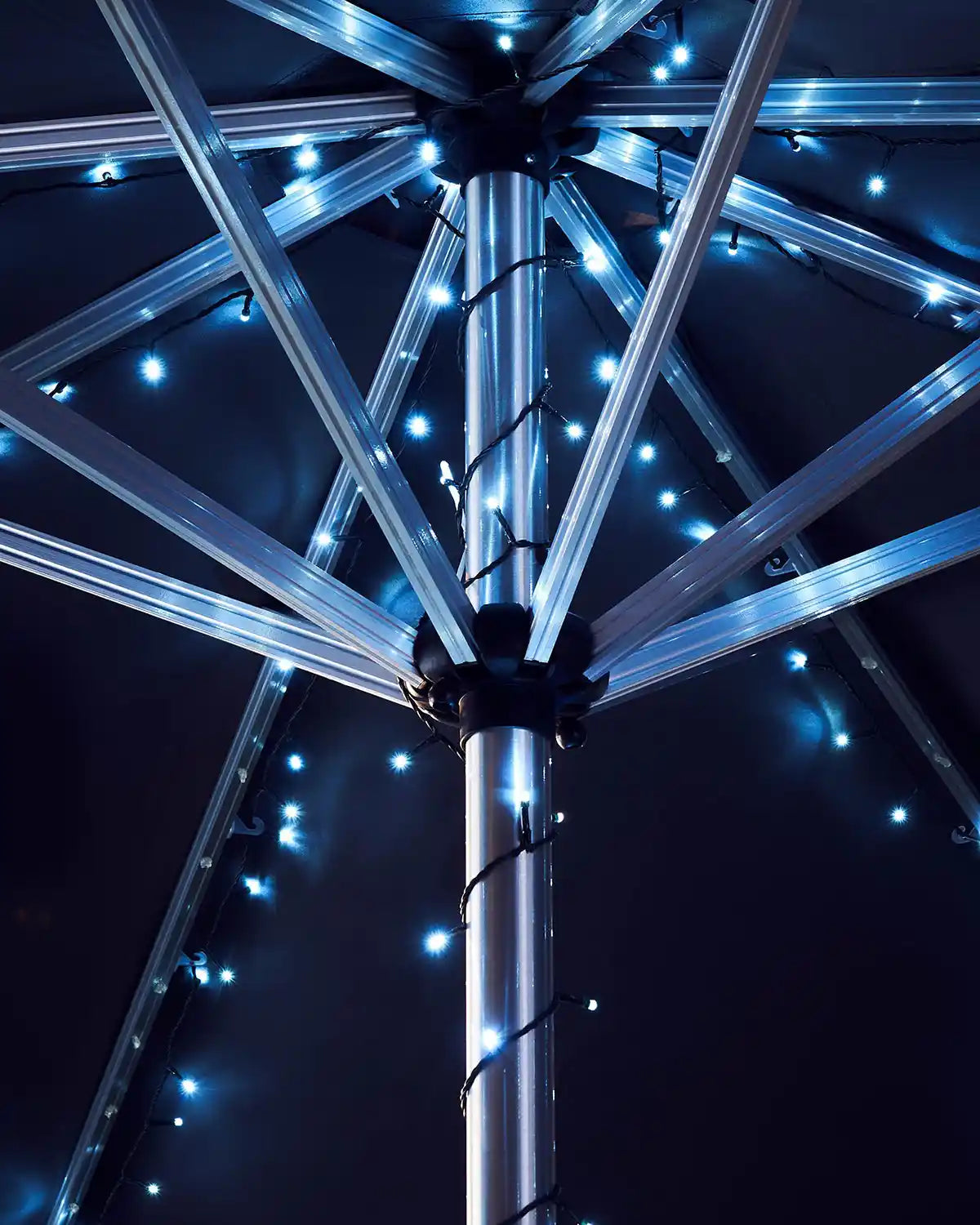 Close-up of a metallic umbrella pole with ice white string lights against a dark background