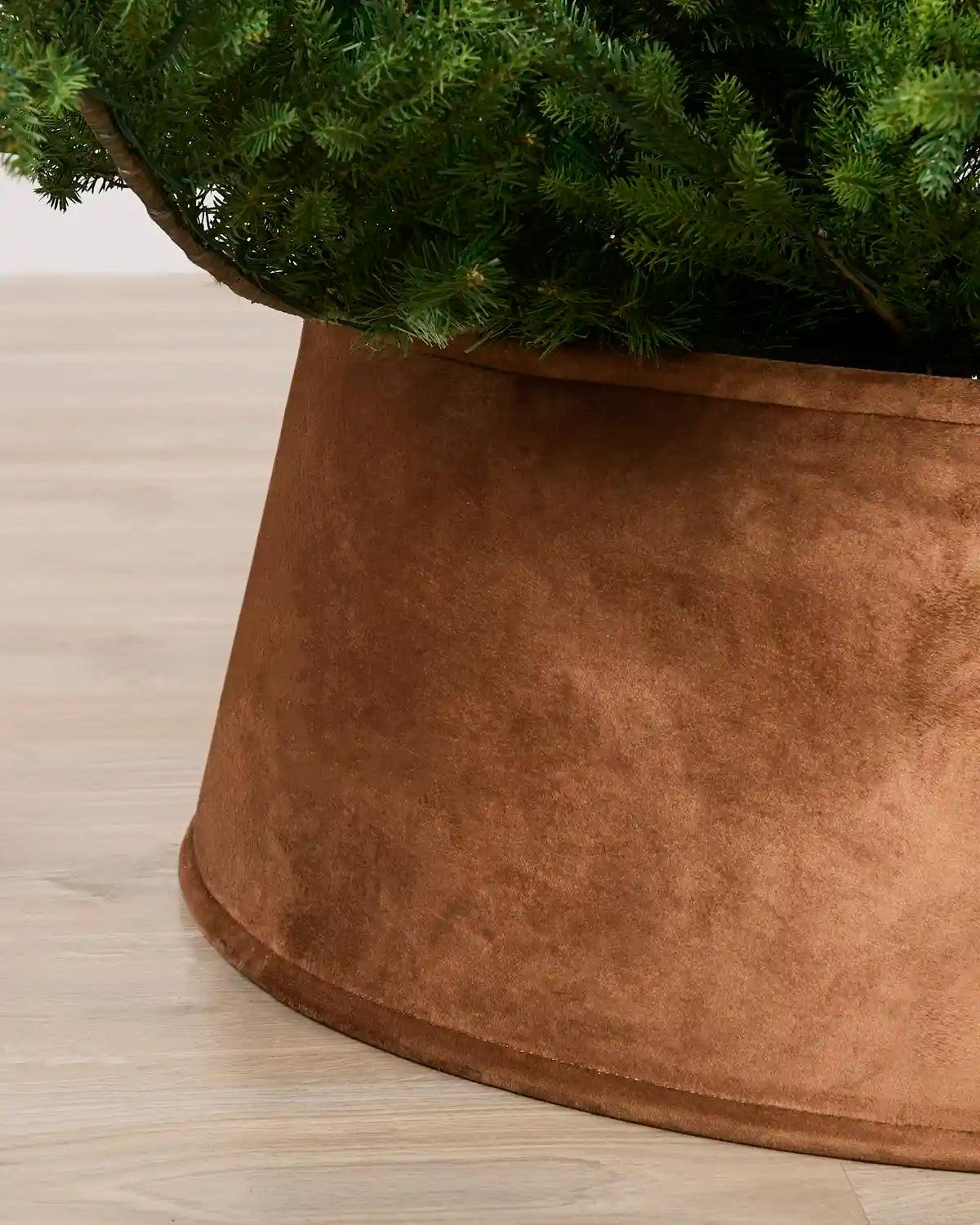 Close-up of a mocha velvet tree skirt holding a green artificial Christmas tree, set on a light wood floor.