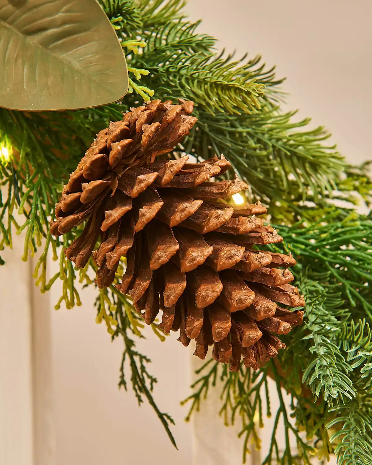 Close-up of a pine cone on a green branch with lights, likely part of a festive decoration.