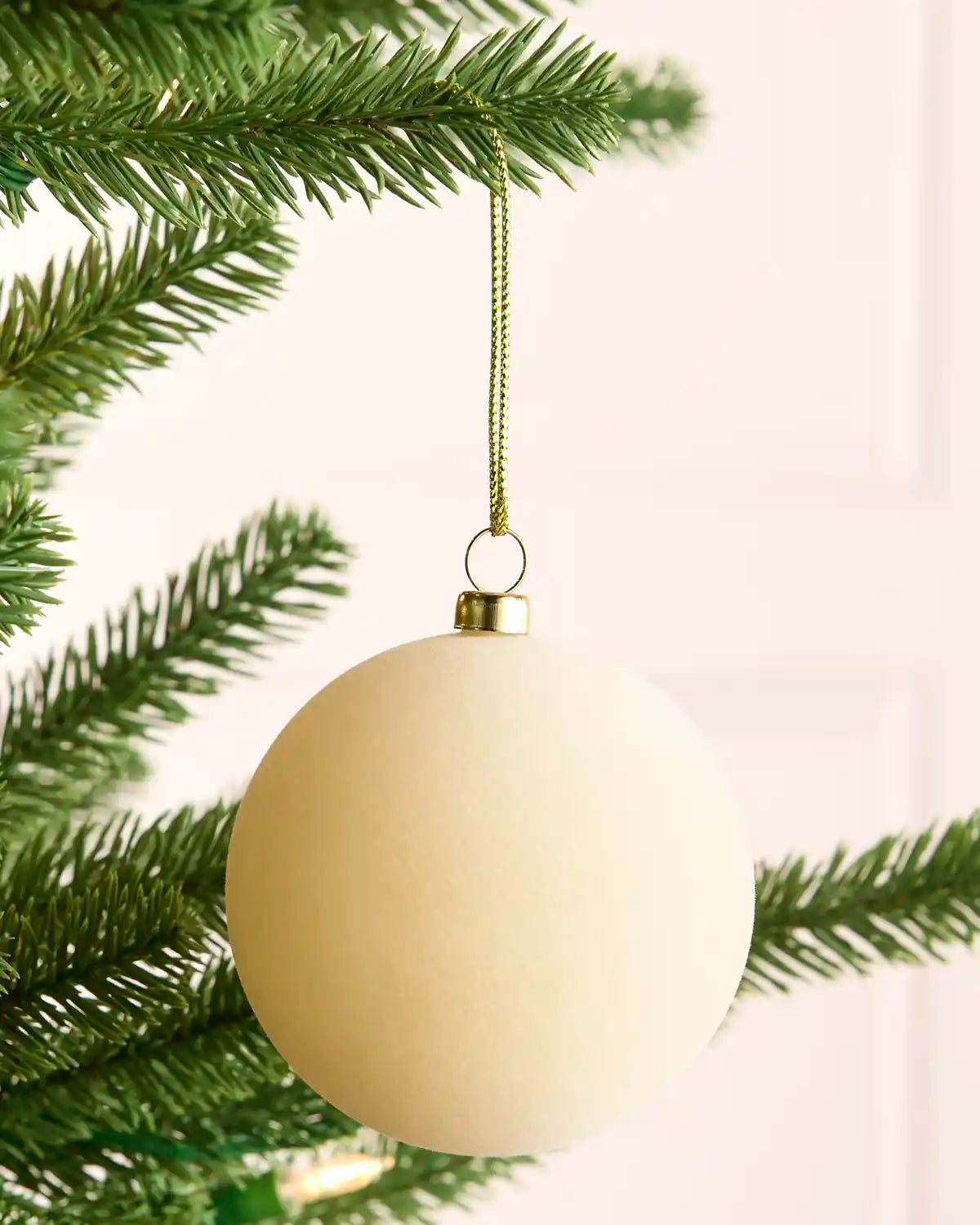 Close-up of a plain, round latte-coloured velvet bauble hanging from a green Christmas tree branch