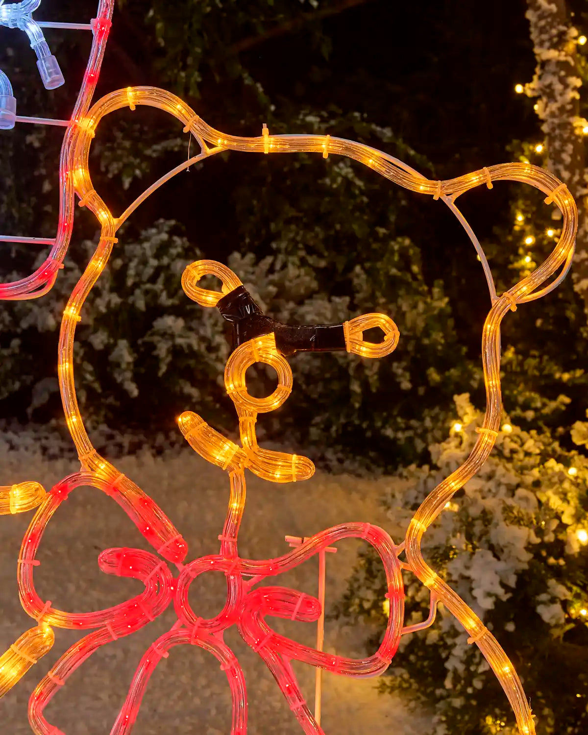 Close-up of a pre-lit teddy bear silhouette with glowing orange rope lights, facial details, and a large red illuminated bow