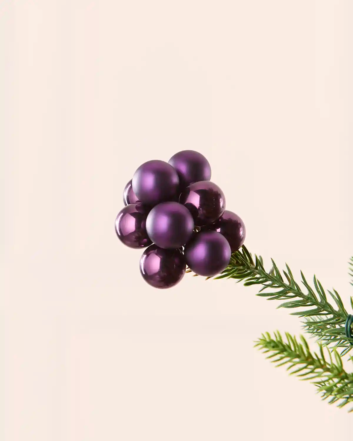 Close-up of a purple glass berry cluster bauble attached to a Christmas tree branch