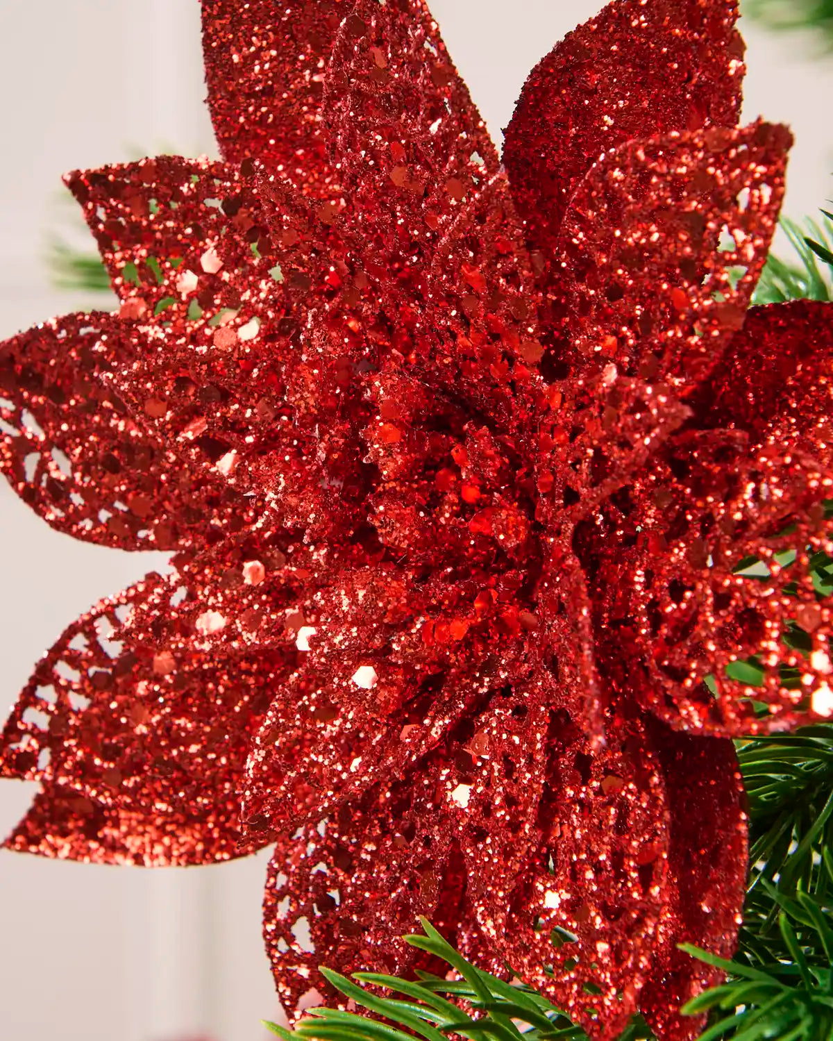 Close-up of a red glitter artificial poinsettia flower showing its densely textured, sparkling petals.

