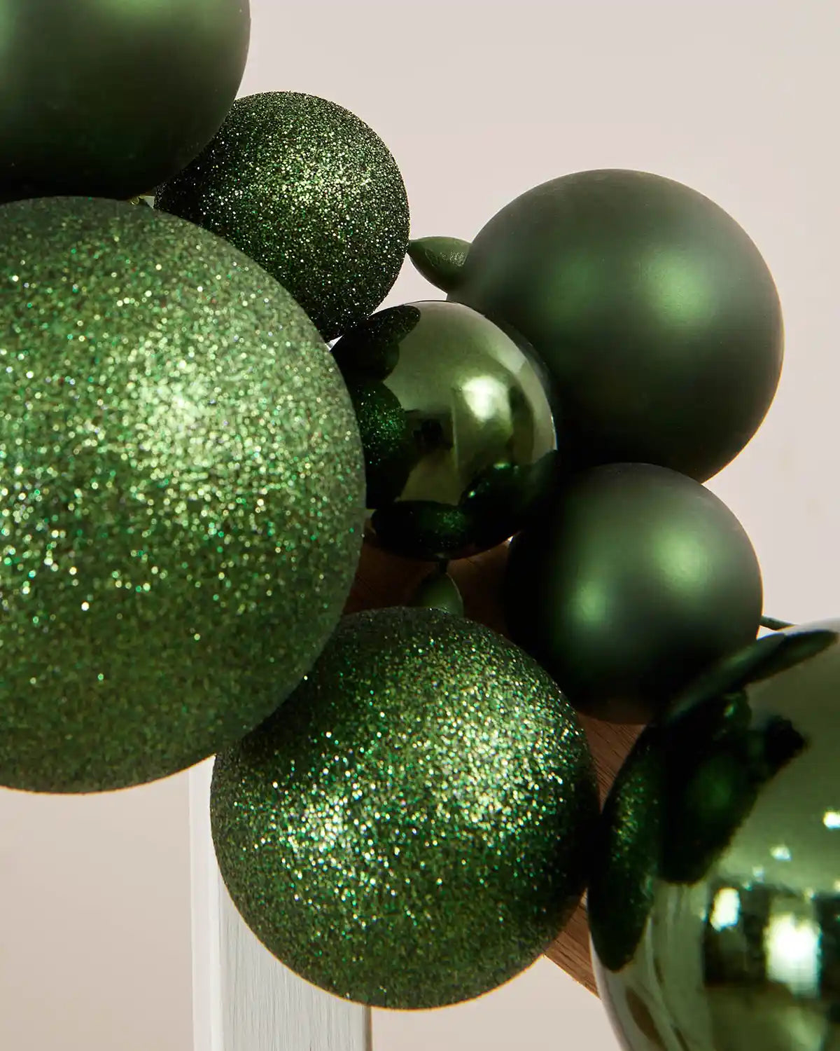 Close-up of a sage green bauble garland on a staircase banister against a cream wall
