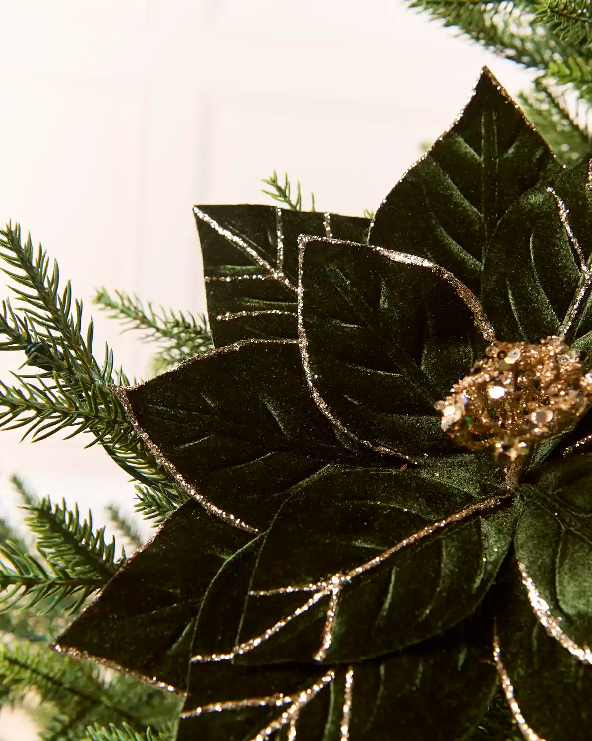 Close-up of a sage green glitter artificial poinsettia flower, highlighting the layered velvet-like petals and gold glitter detailing along the edges and veins