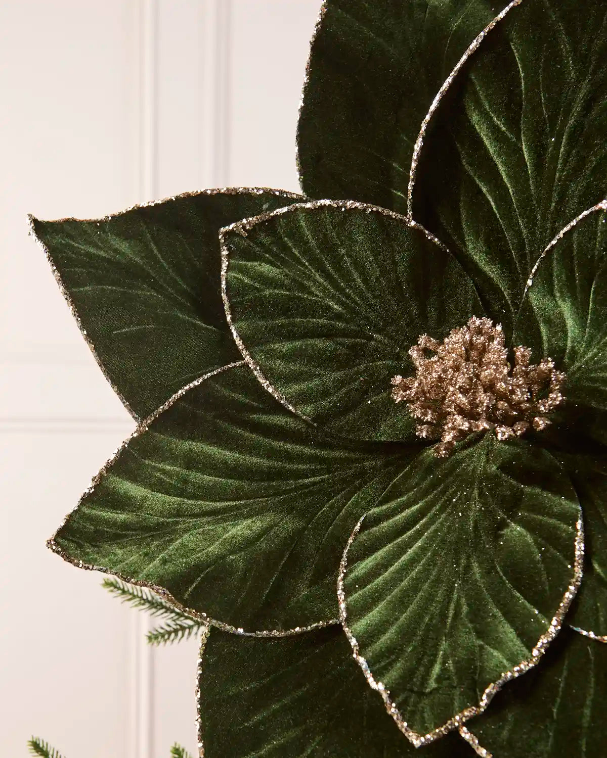 Close-up of a sage green velvet artificial poinsettia, highlighting its soft texture, detailed petal veining and glittered edges.
