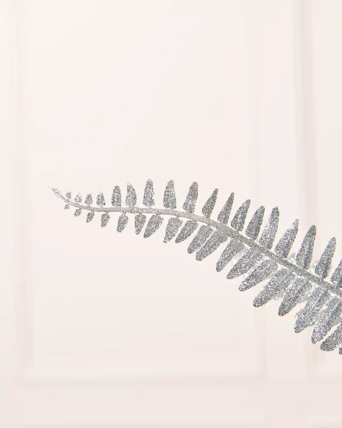 Close-up of a silver glitter leaf spray featuring a single glitter-covered leafy stem against a white background.