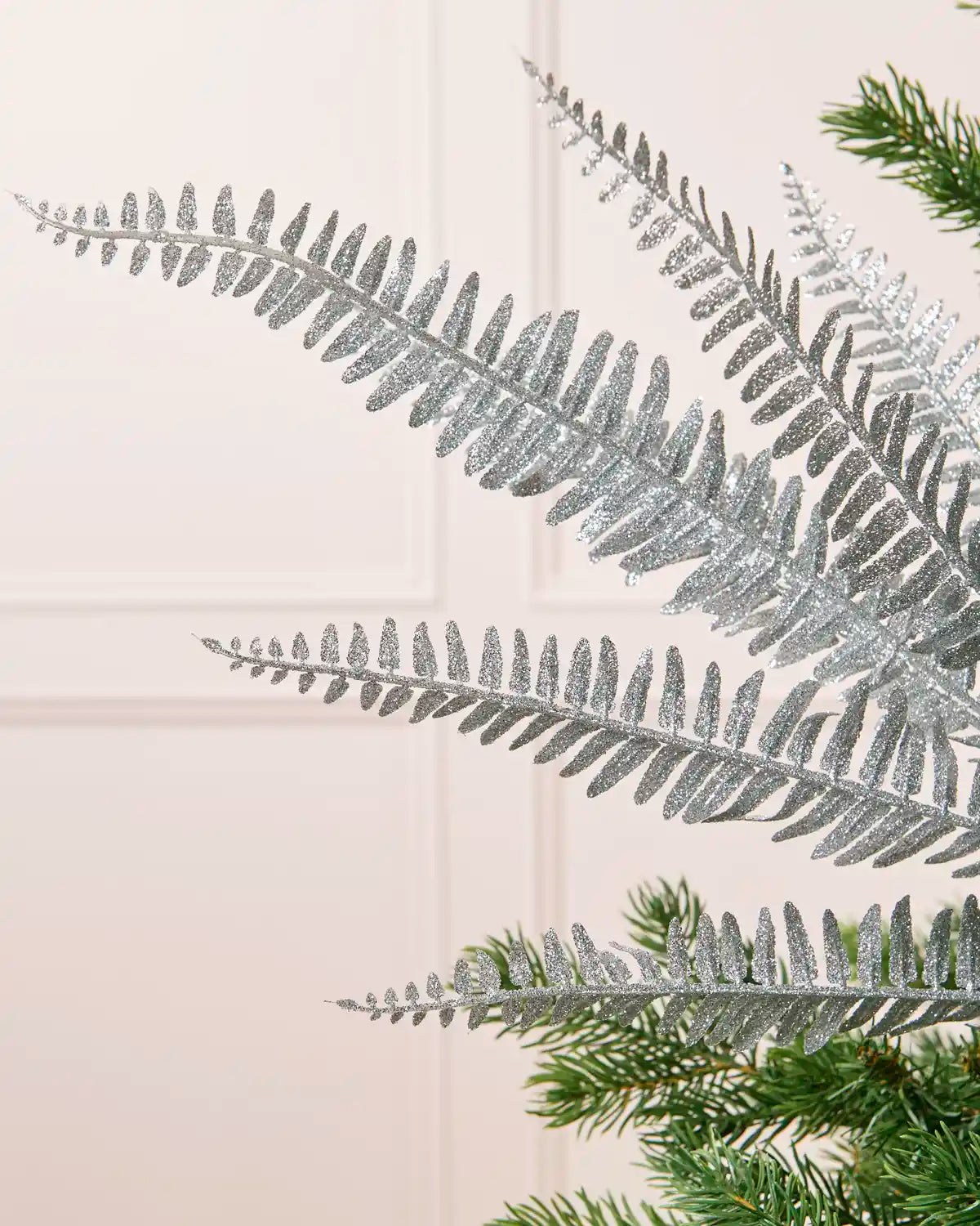 Close-up of a silver glitter leaf spray featuring detailed glitter-covered leaves and branches with Christmas tree branches in the background