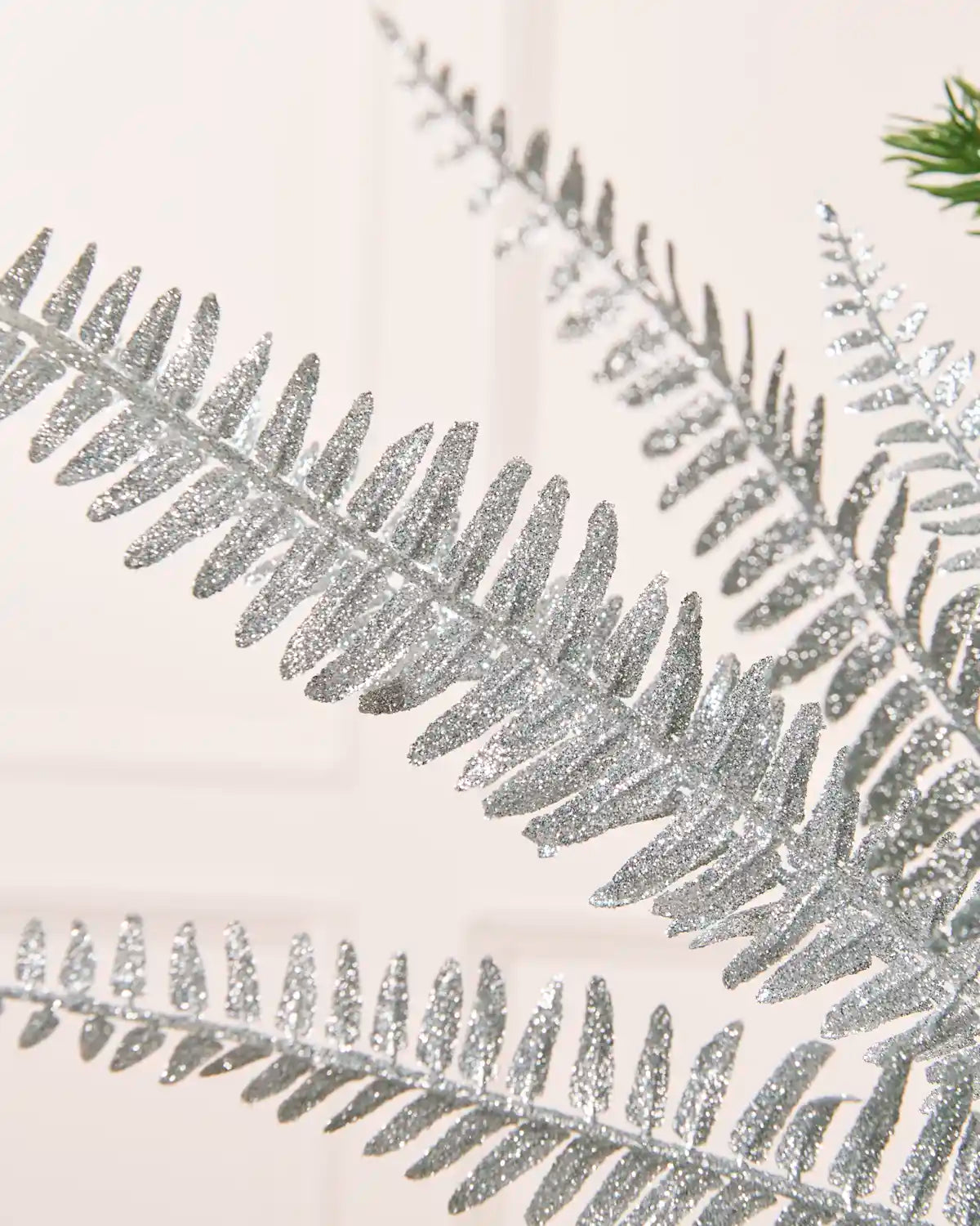 Close-up of a silver glitter leaf spray showing a detailed glitter-covered branch with narrow leaves against a white background