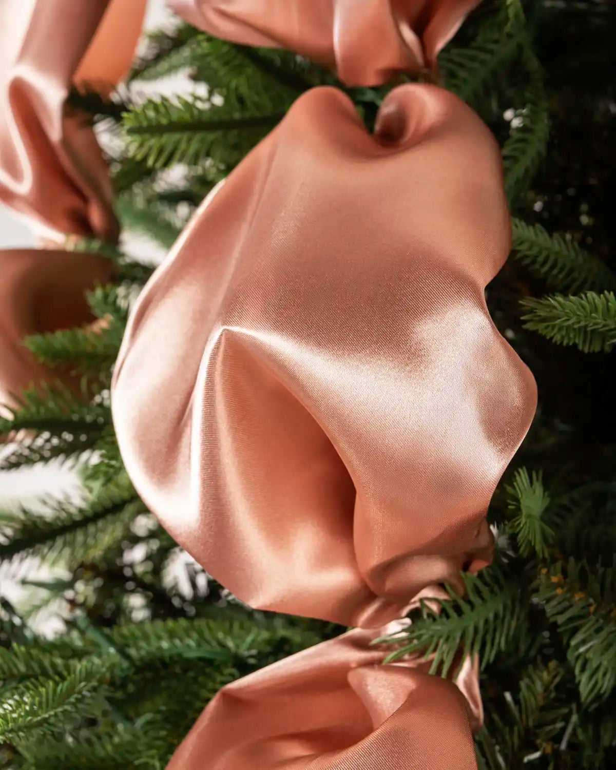 Close-up of a soft rose gold satin ribbon draped over green Christmas tree branches