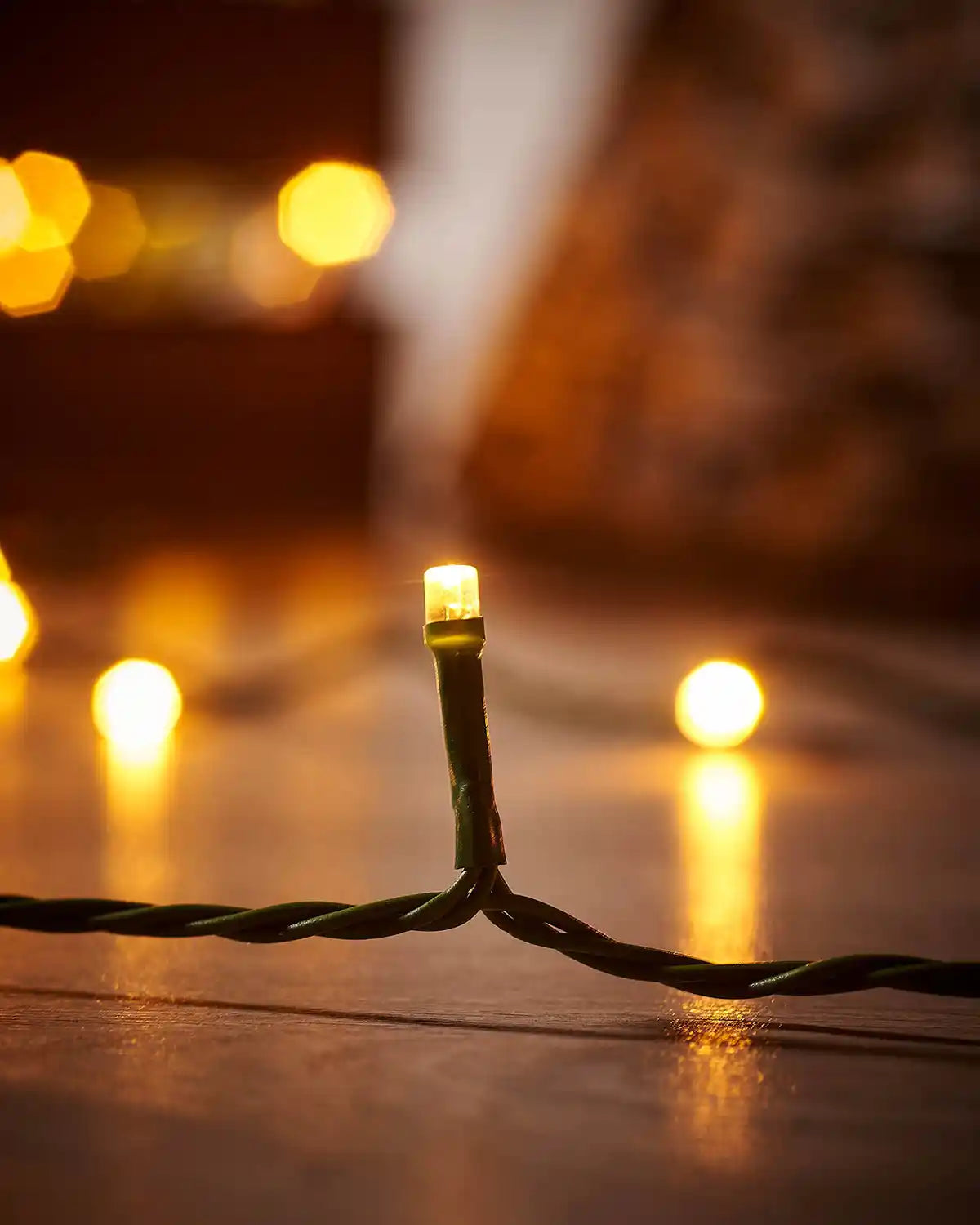Close-up of a string of Christmas lights on a wooden surface with blurred Tree collar in the background.