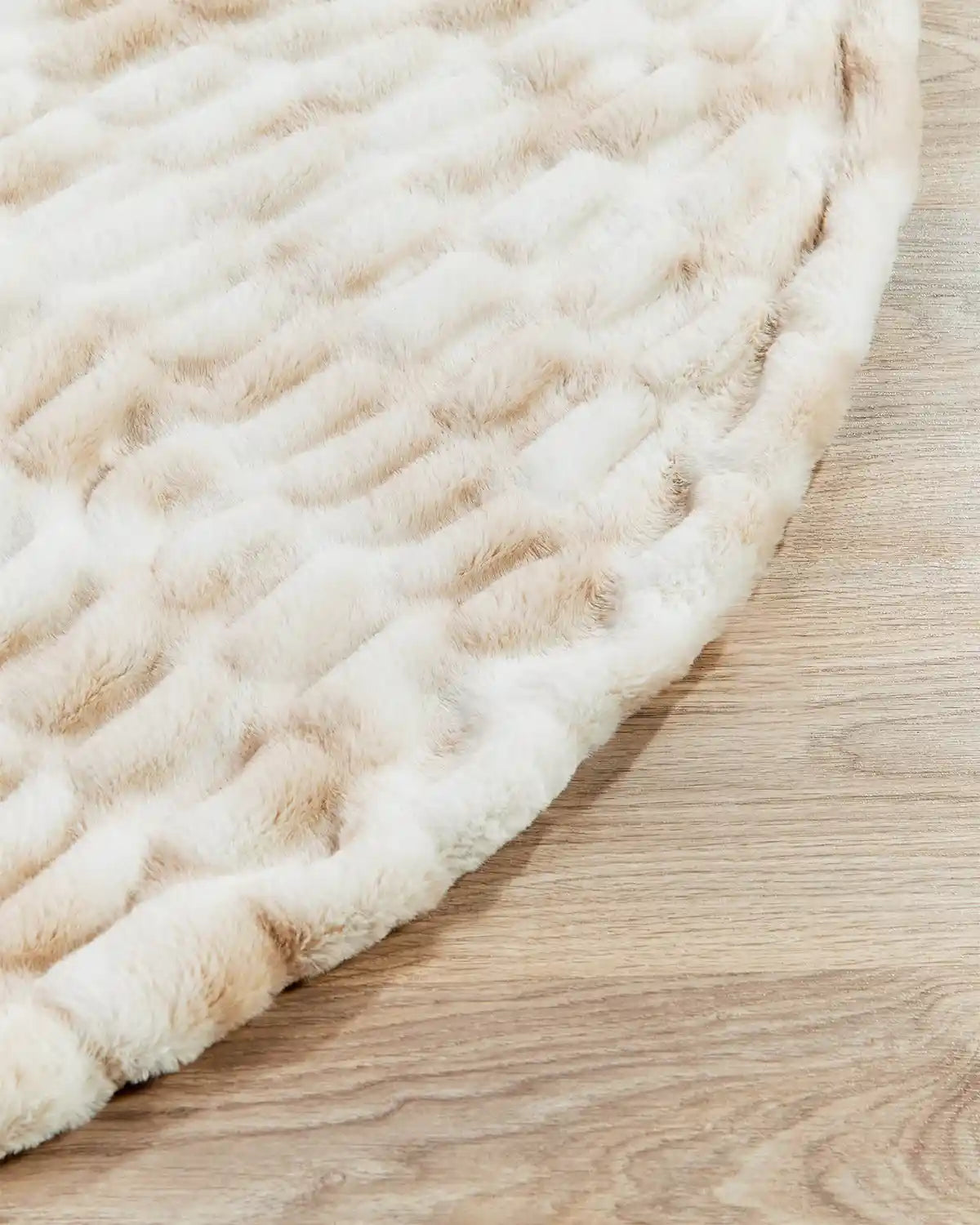 Close-up of a textured beige and white Christmas tree skirt on a wooden floor