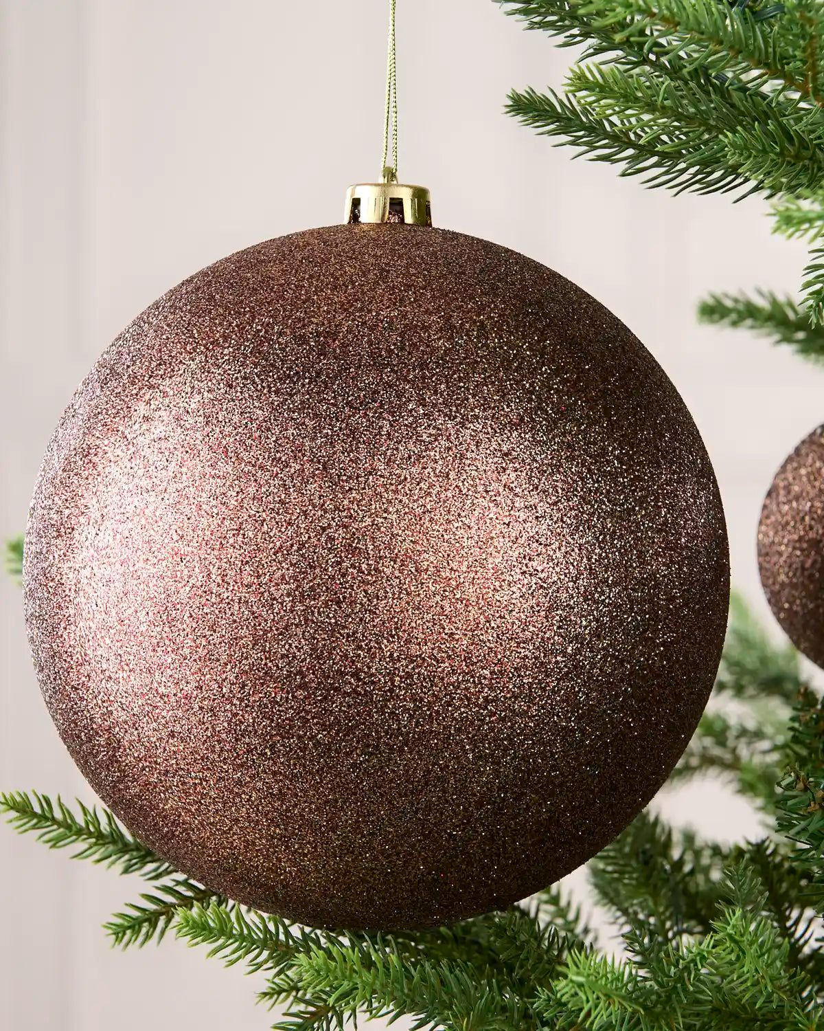 Close-up of an Espresso 20 cm oversized shatterproof bauble with a Glitter finish on a Christmas tree.
