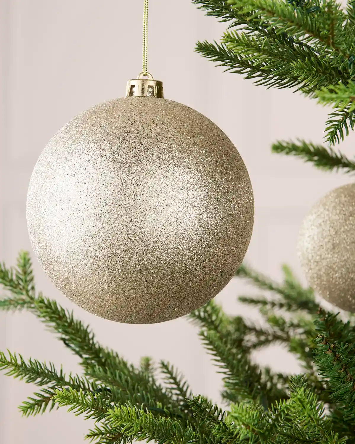 Close-up of an Latte 15 cm oversized shatterproof bauble with a glitter finish on a Christmas tree.

