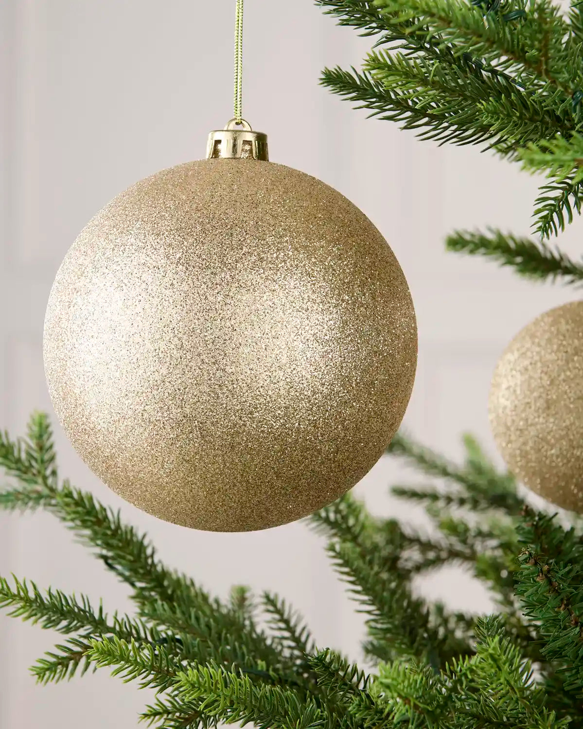 Close-up of an Latte 15 cm oversized shatterproof bauble with a glitter finish on a Christmas tree.
