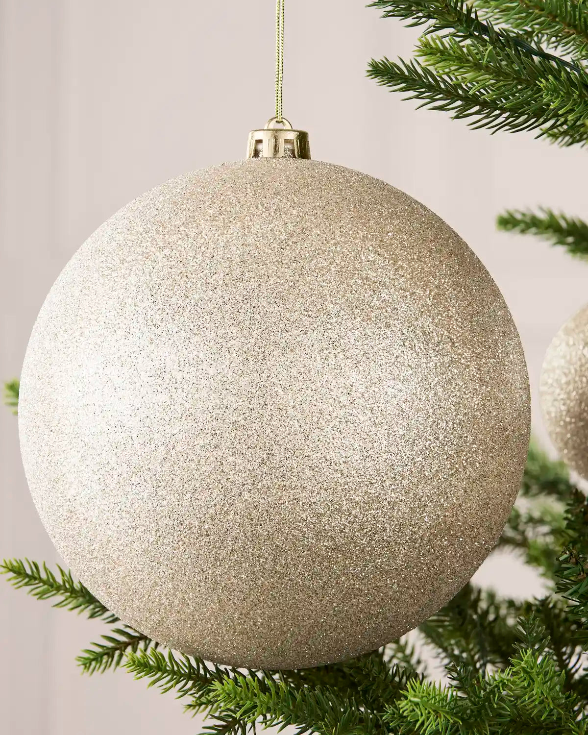 Close-up of an Latte 20 cm oversized shatterproof bauble with a glitter finish on a Christmas tree.
