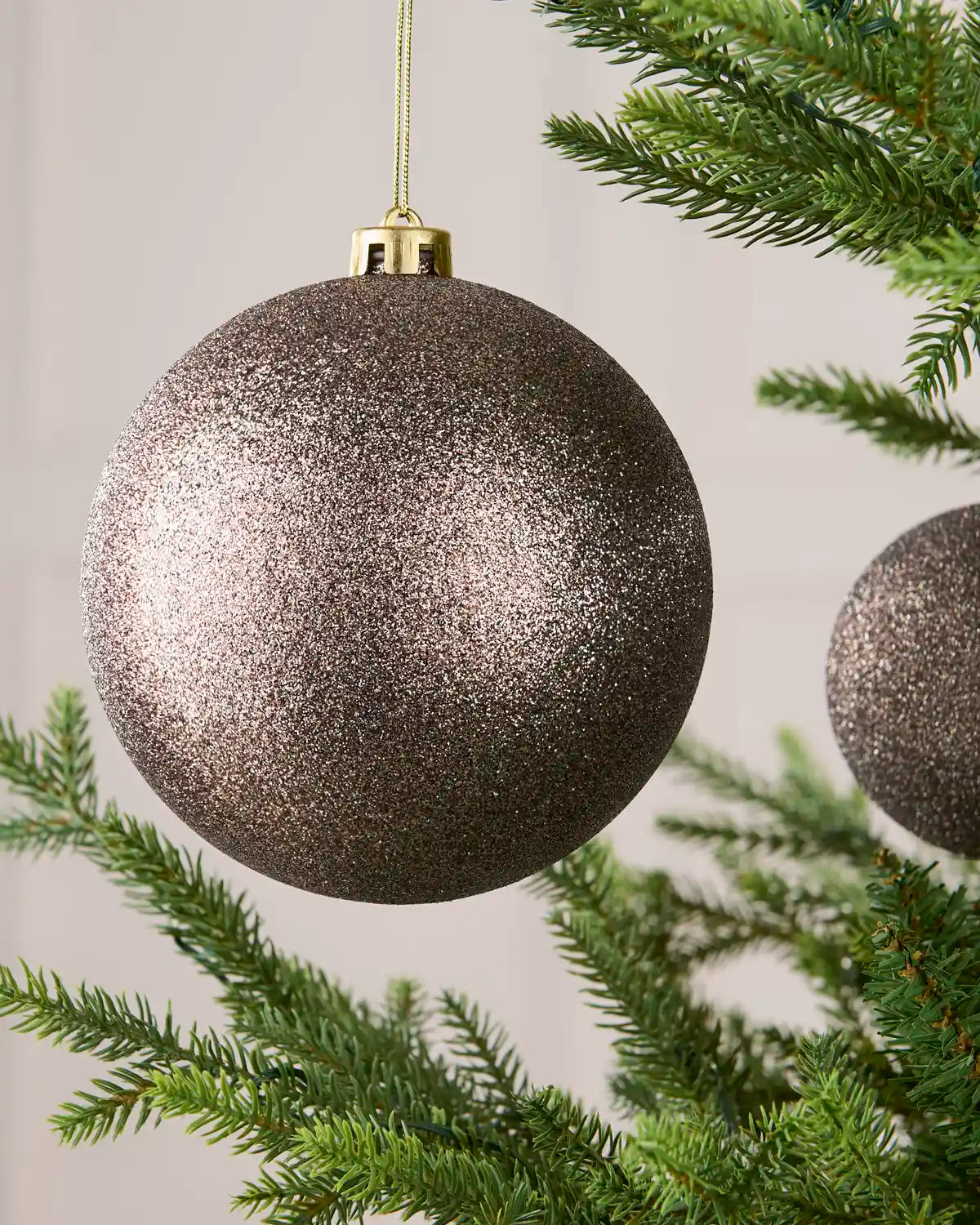 Close-up of an Mocha 15 cm oversized shatterproof bauble with a Glitter finish on a Christmas tree.
