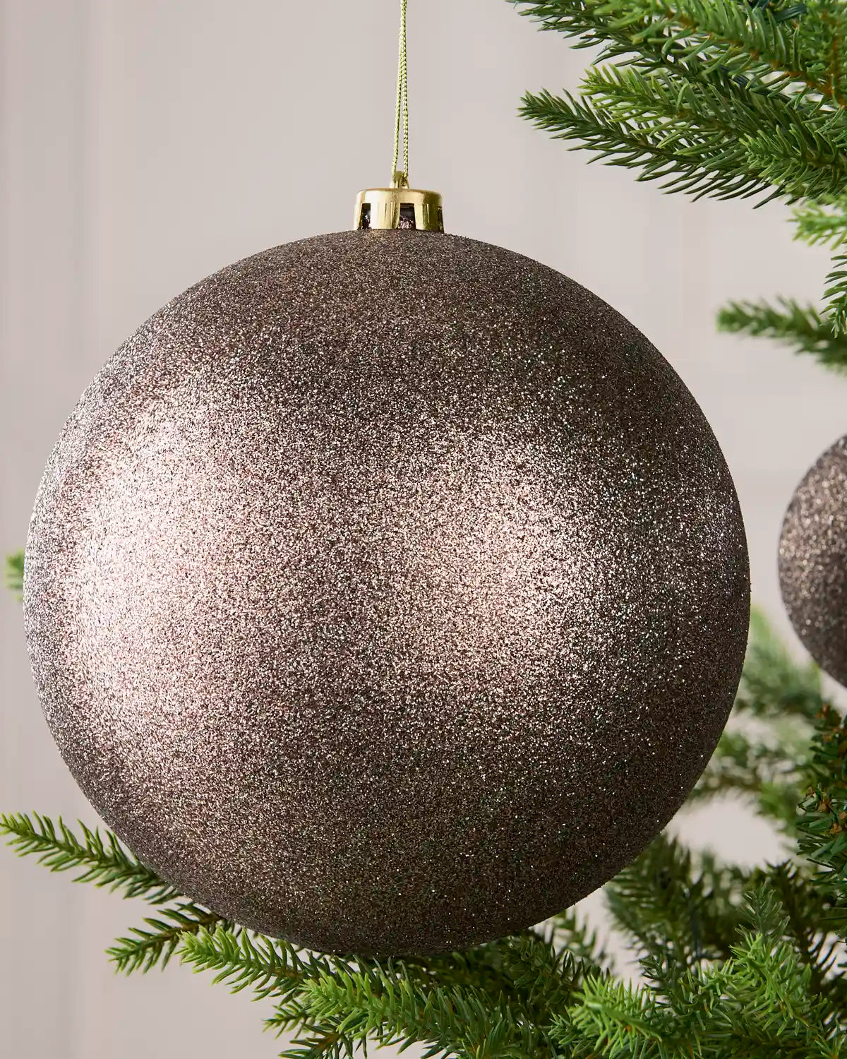 Close-up of an Mocha 20 cm oversized shatterproof bauble with a Glitter finish on a Christmas tree.
