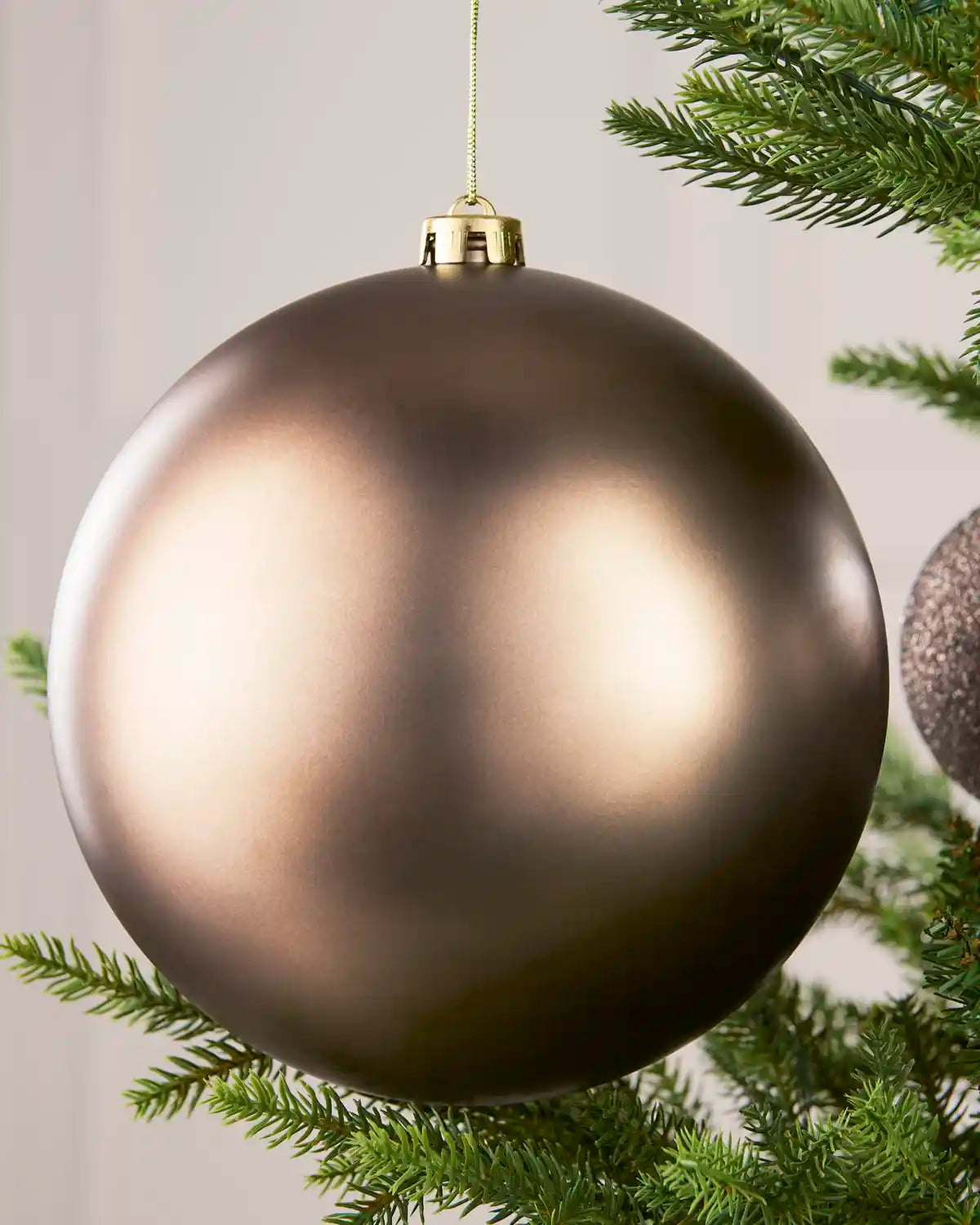 Close-up of an Mocha 20 cm oversized shatterproof bauble with a Matt finish on a Christmas tree.
