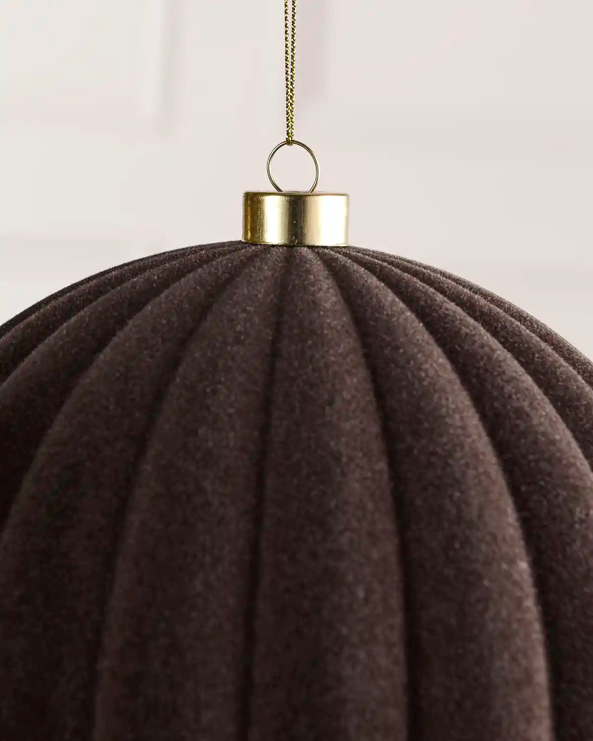 Close-up of an espresso coloured pleated fabric hanging ornament with a gold metal cap and hanging chain.