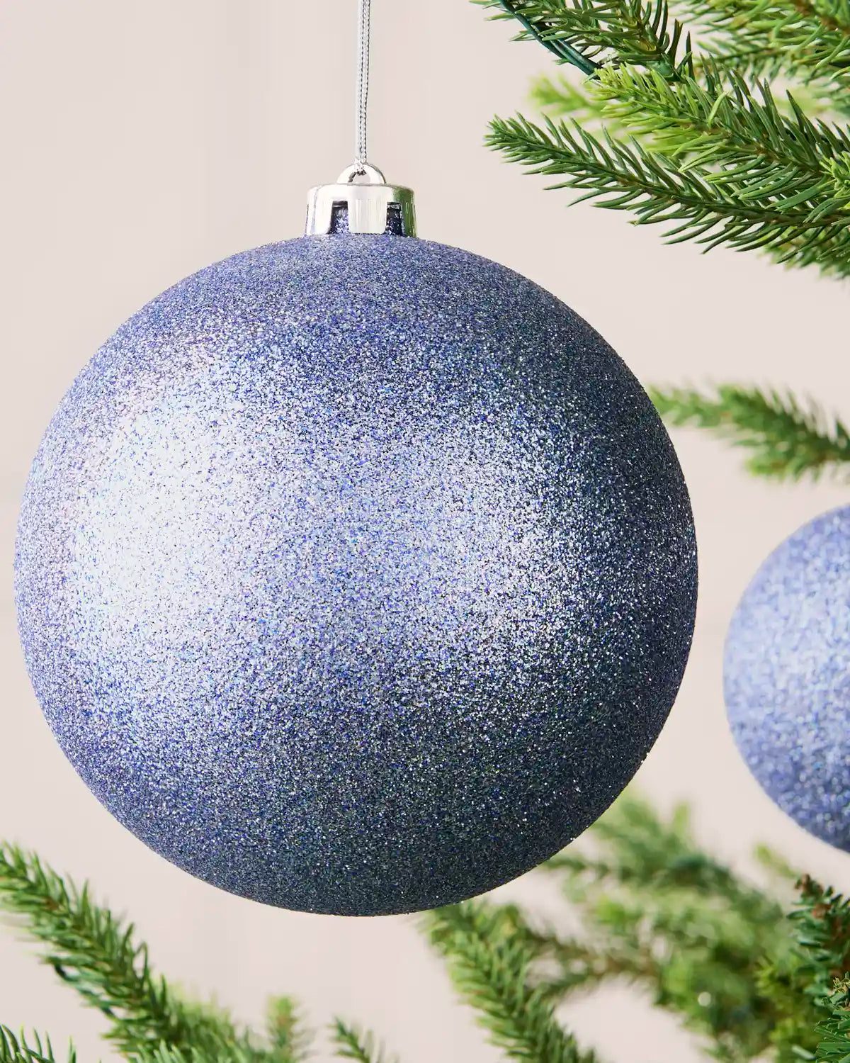 Close-up of an ice blue 15 cm oversized shatterproof bauble with a glitter finish on a Christmas tree.
