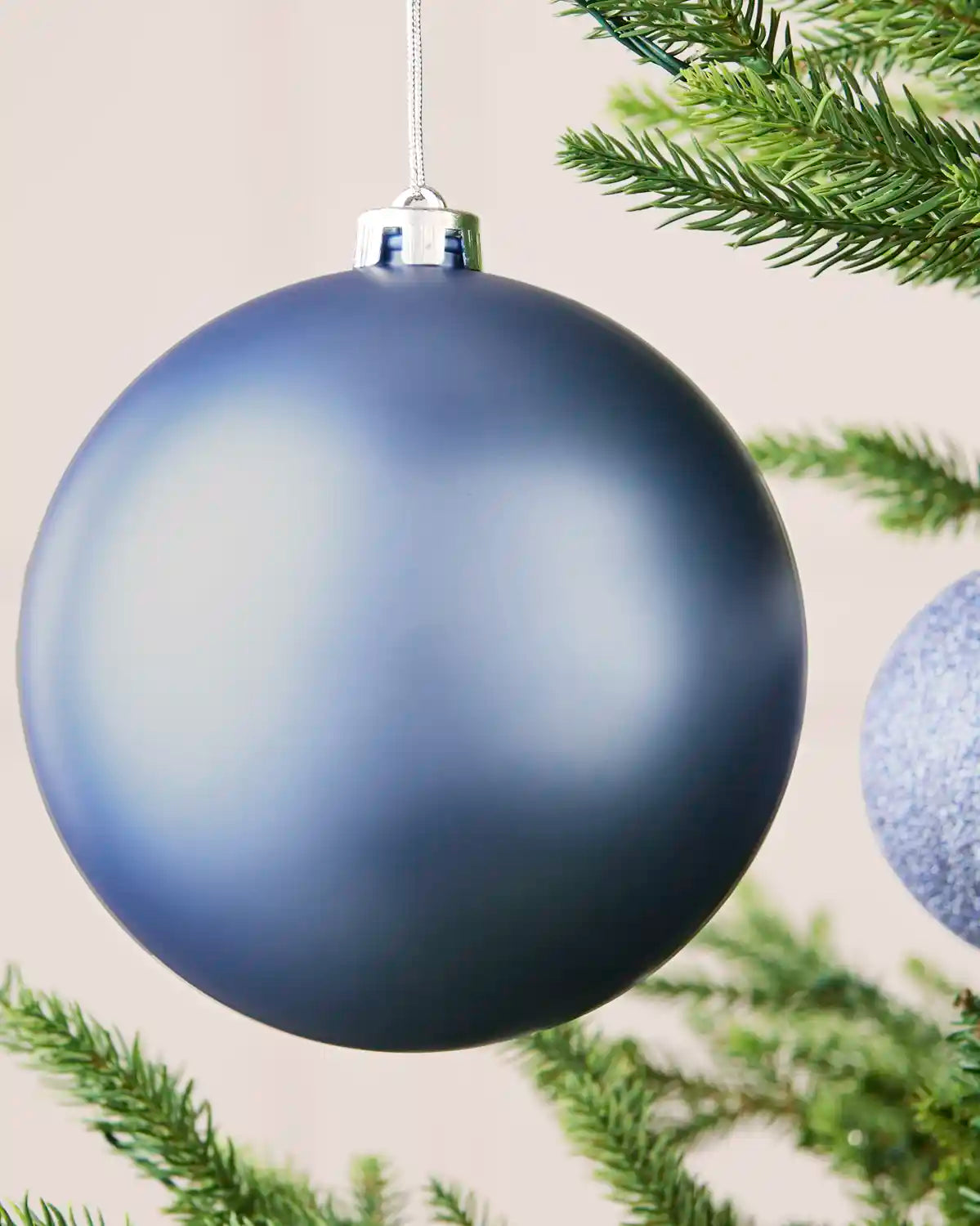 Close-up of an ice blue 15 cm oversized shatterproof bauble with a smooth matt finish on a Christmas tree.
