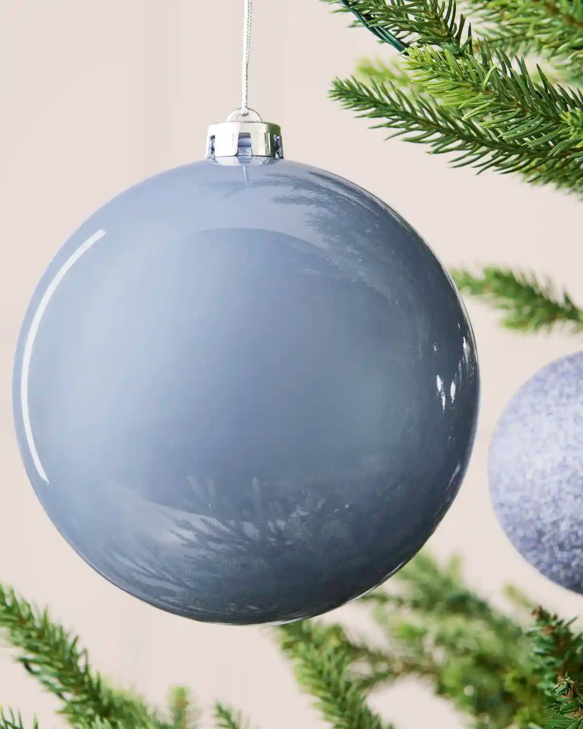 Close-up of an ice blue 15 cm oversized shatterproof bauble with a smooth shiny finish on a Christmas tree.
