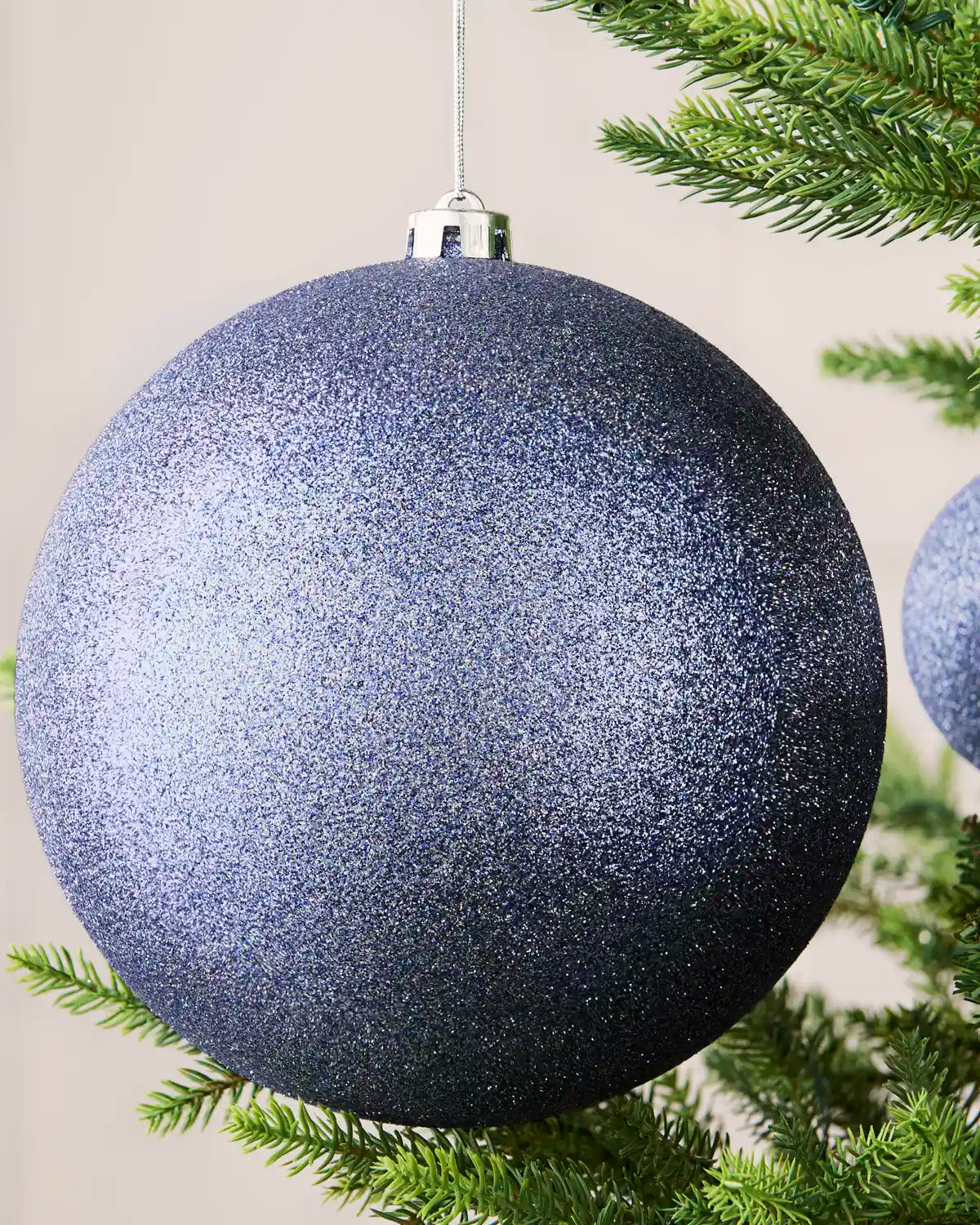 Close-up of an ice blue 20 cm oversized shatterproof bauble with a glitter finish on a Christmas tree.
