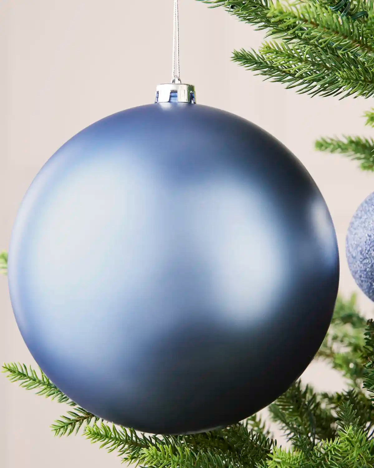 Close-up of an ice blue 20 cm oversized shatterproof bauble with a smooth matt finish on a Christmas tree.
